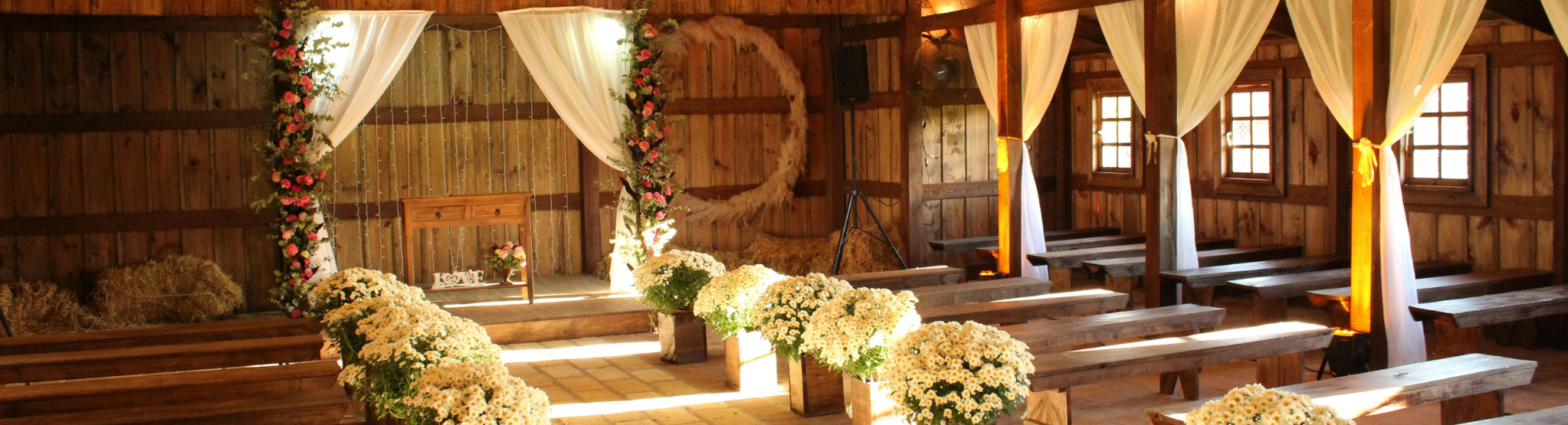 A rustic barn wedding venue with white curtains and a warm golden glow.