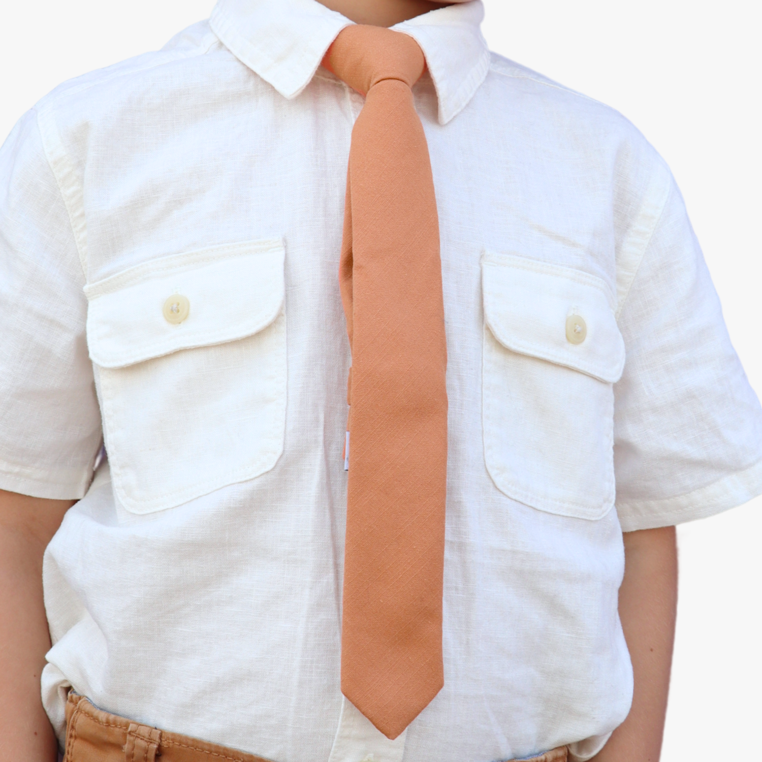 The torso of a boy wearing a solid kids tie with plain burnt orange salmon color.