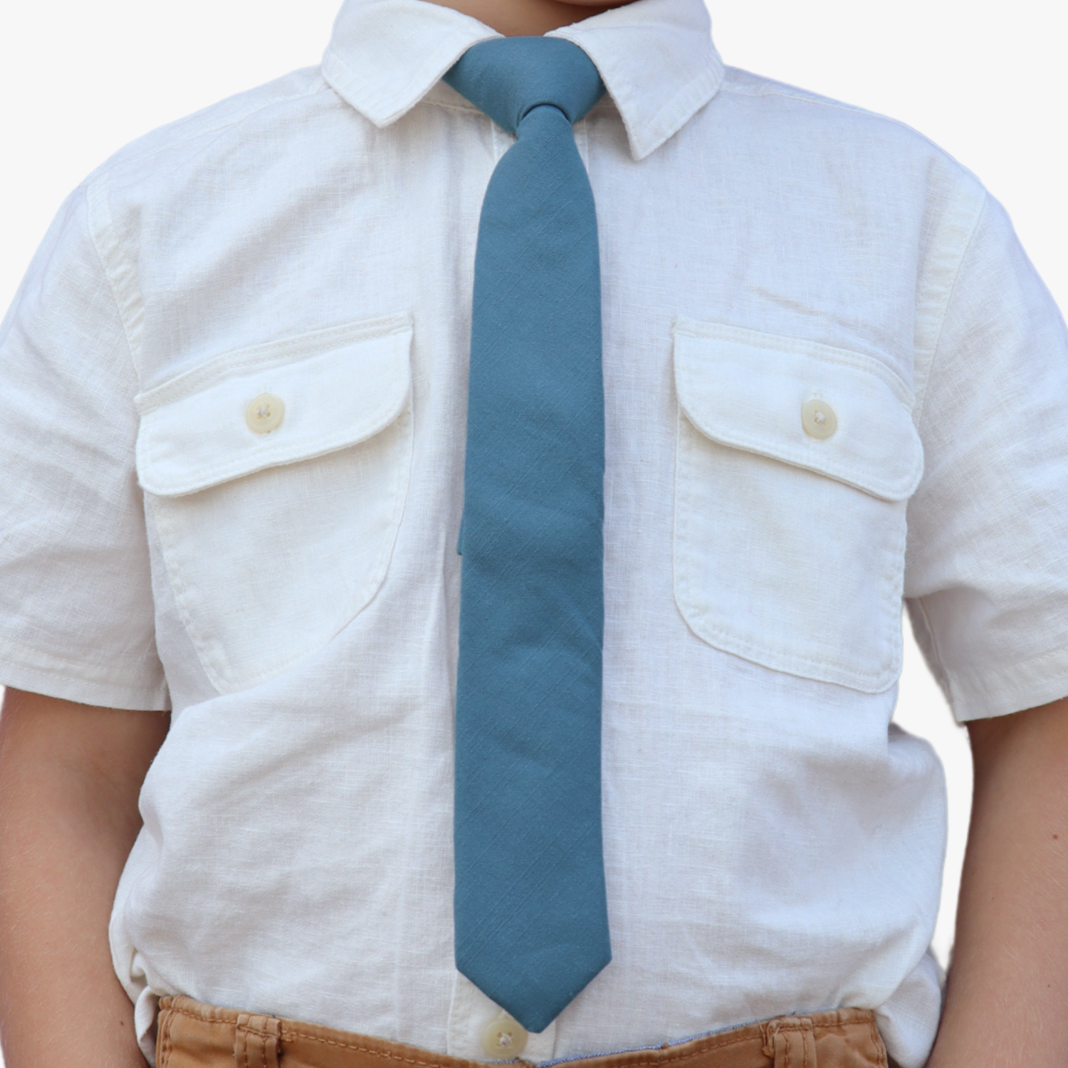 The torso of a boy wearing a solid kids tie with plain deep cobalt blue color.