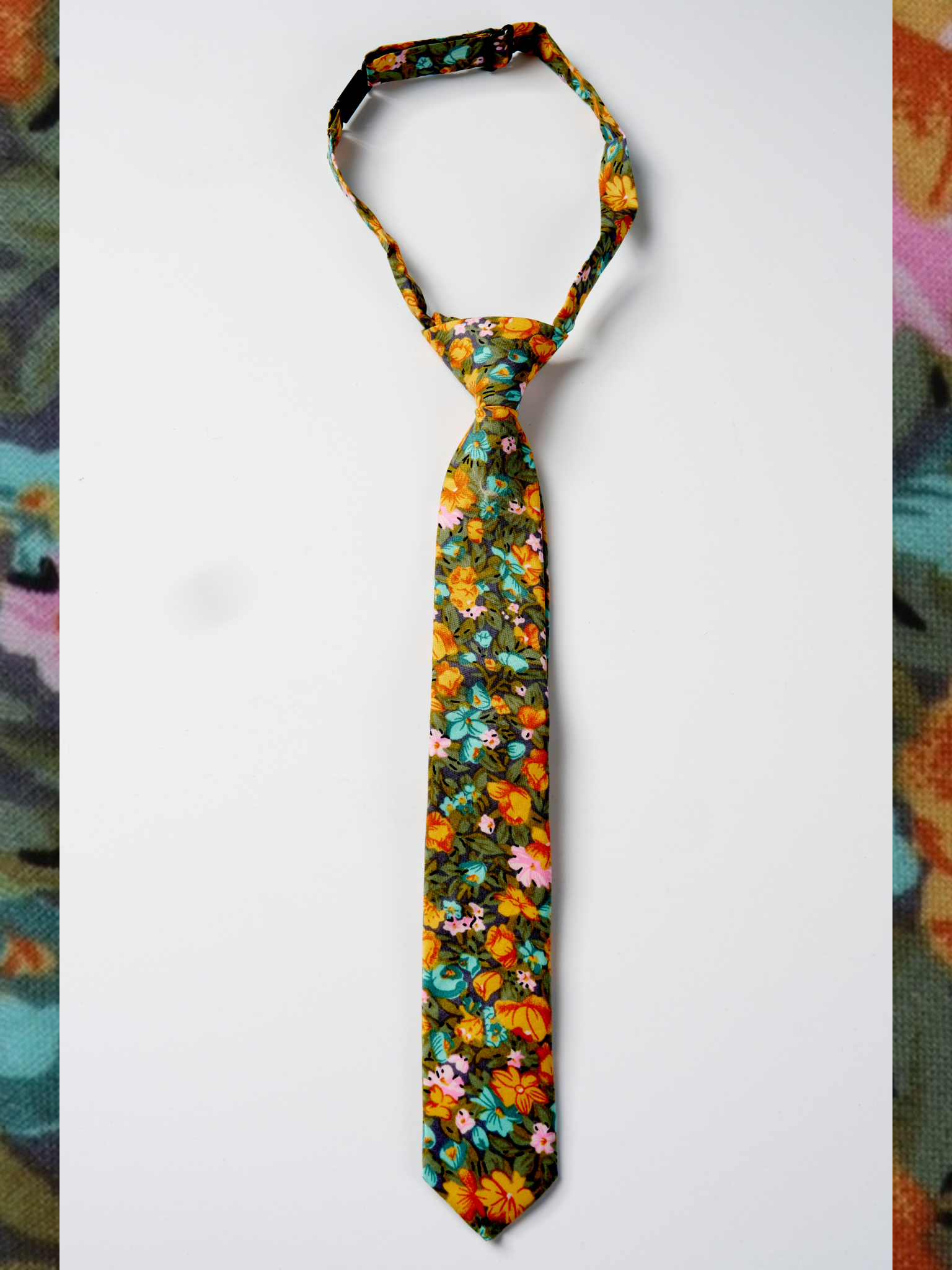 A folded woven cotton, floral men's tie with orange flowers, dark pletals, light blue blossoms and green leaves.