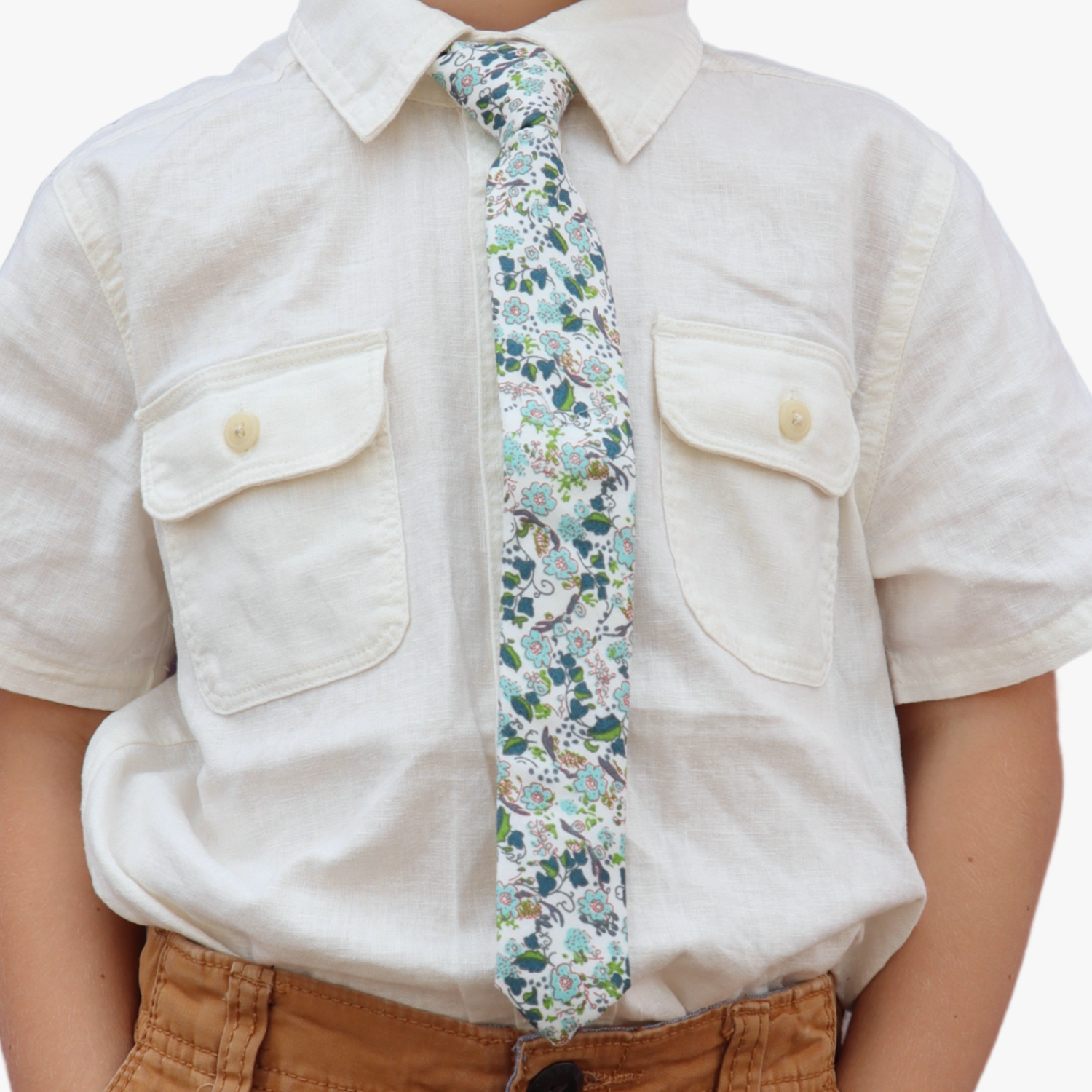 The torso of a boy wearing a floral kids tie with dusty blue flowers, pink accents, turquoise blossoms and bluish leaves.