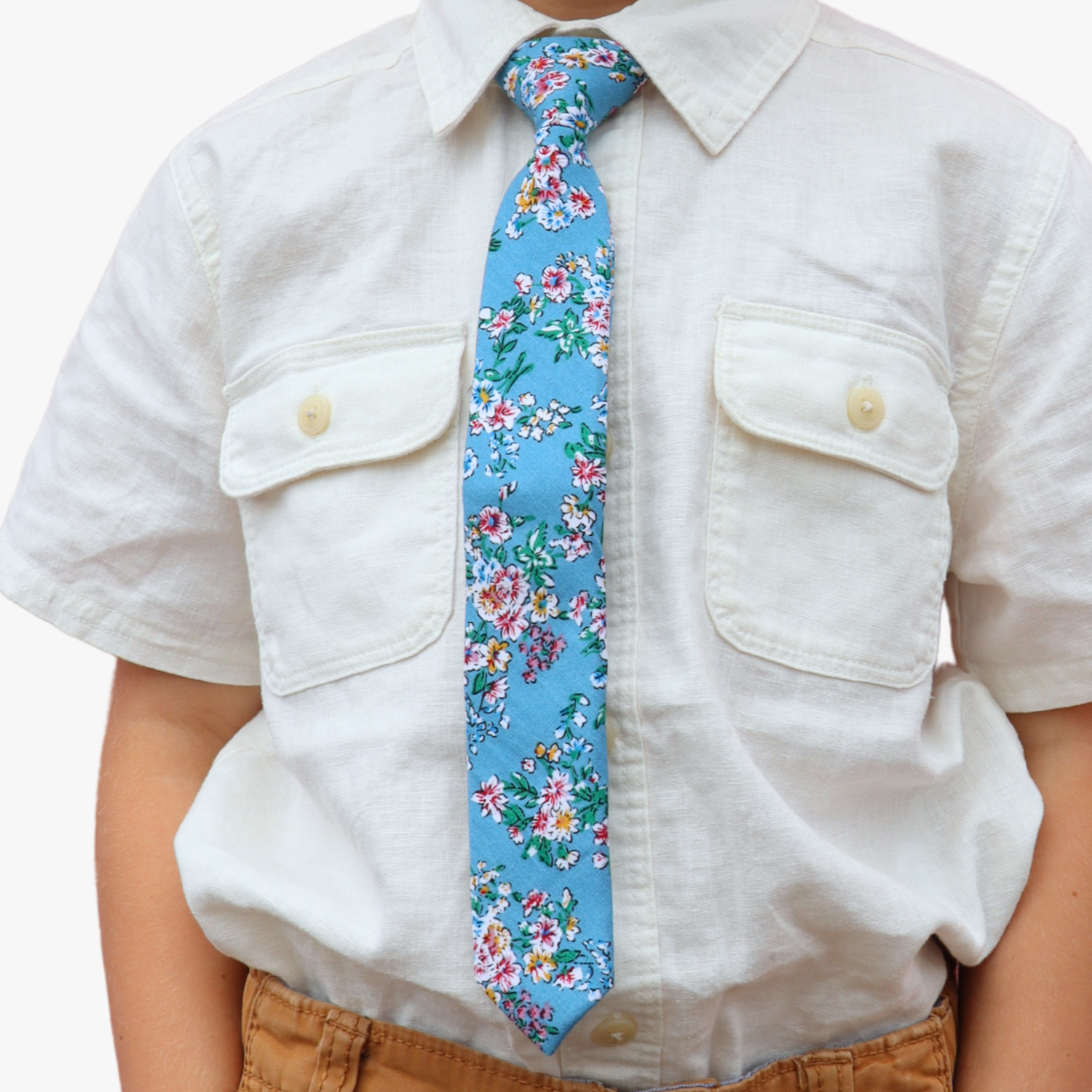 The torso of a boy wearing a floral kids tie with watercolor turqouise flowers, pink and yellow blossoms, and green leaves.
