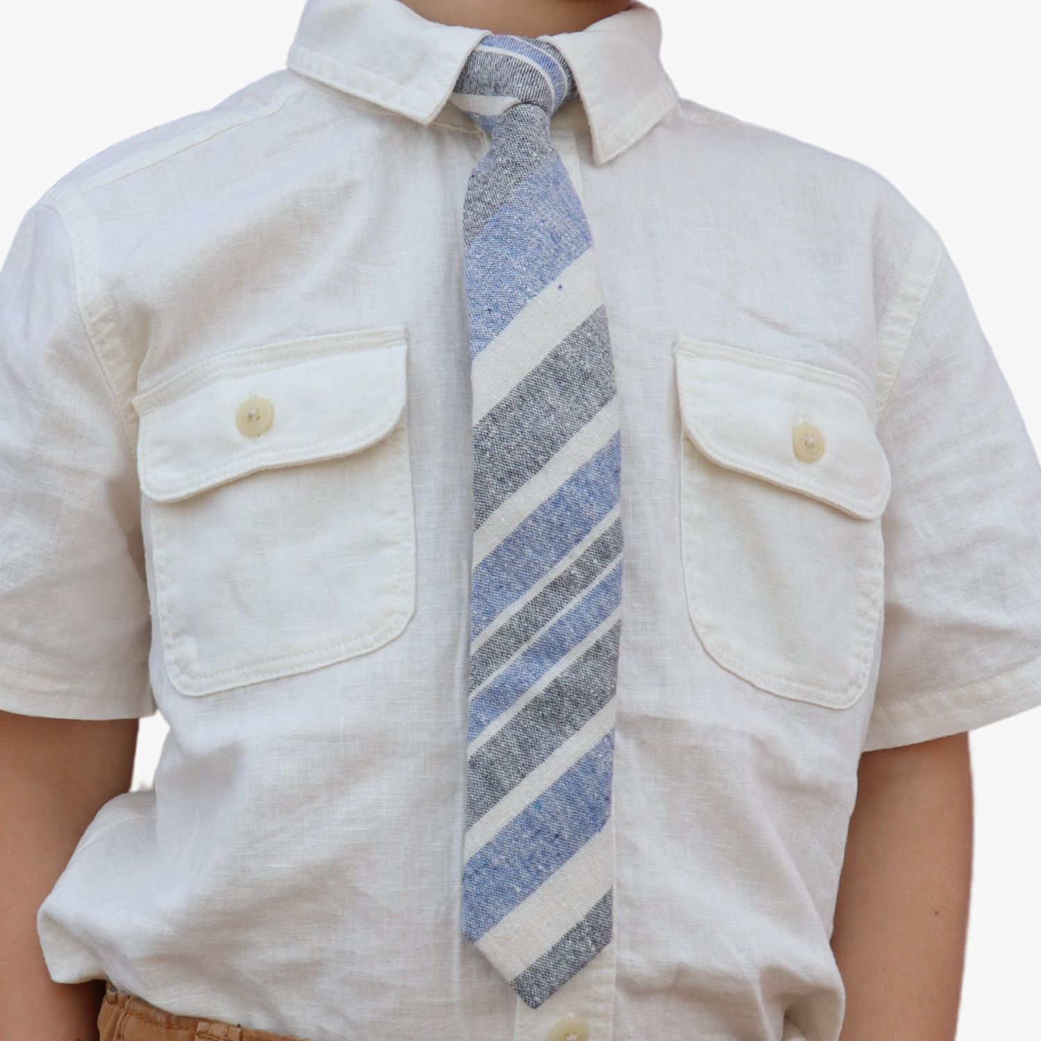 The torso of a boy wearing a striped kids tie with denim blue stripes, beige cream lines, grey bars and diagonal designs.