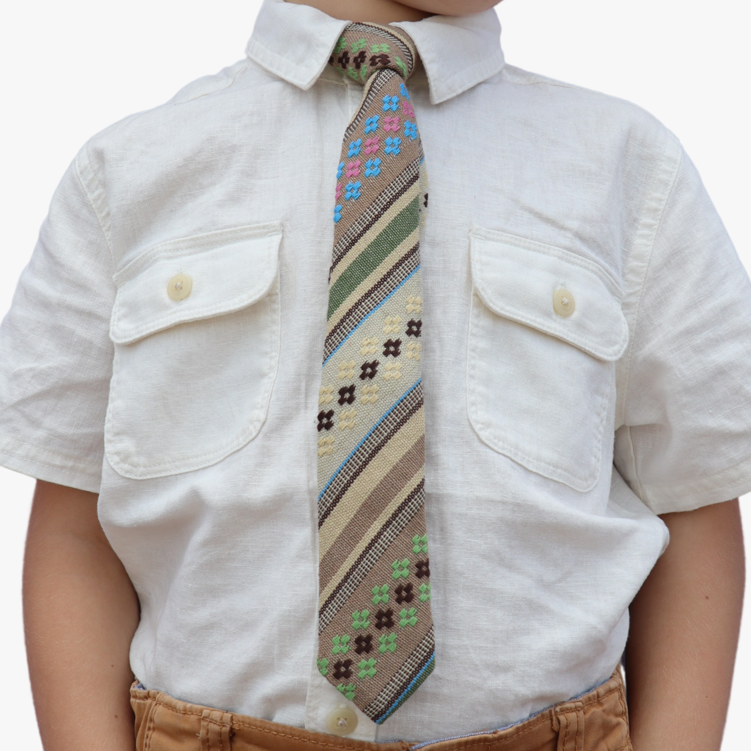 The torso of a boy wearing a striped kids tie with green stripes, tan lines, brown bars and cross designs.