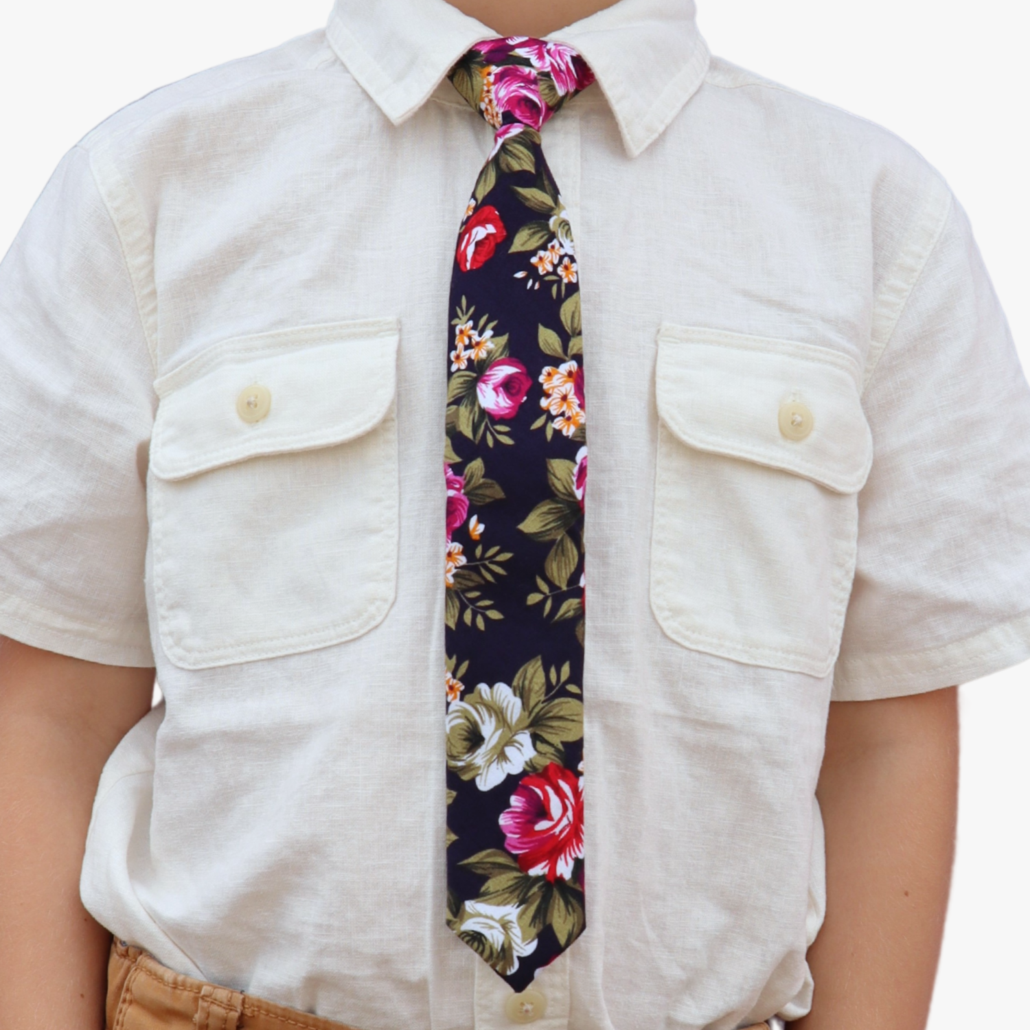The torso of a boy wearing a floral kids tie with pink rose flowers, red petals, yellow blossoms and green leaves.