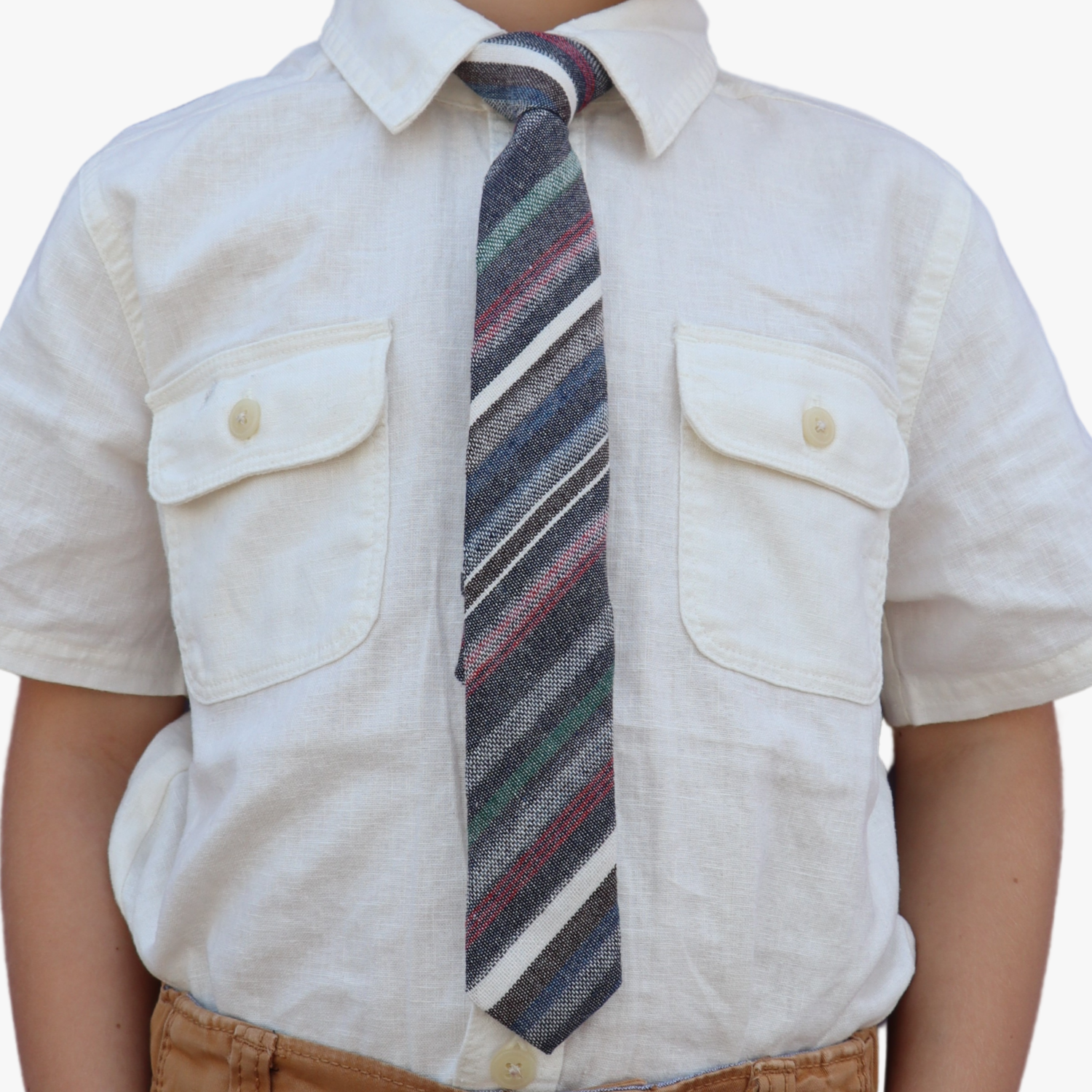 The torso of a boy wearing a striped kids tie with dark gray stripes, thin red lines, light grey bars and diagonal designs.