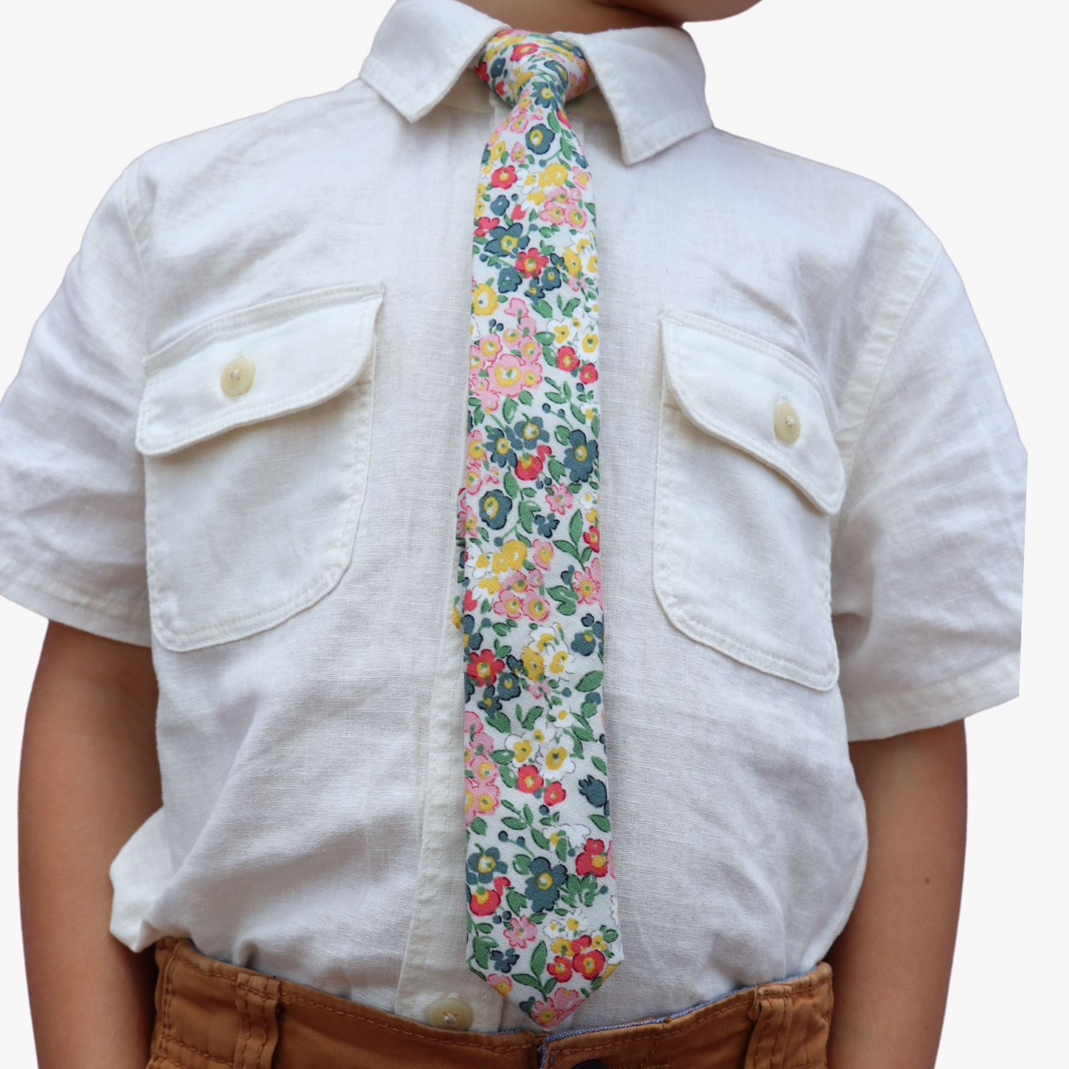The torso of a boy wearing a floral kids tie with small pink flowers, teal petals, yellow blossoms and green leaves.