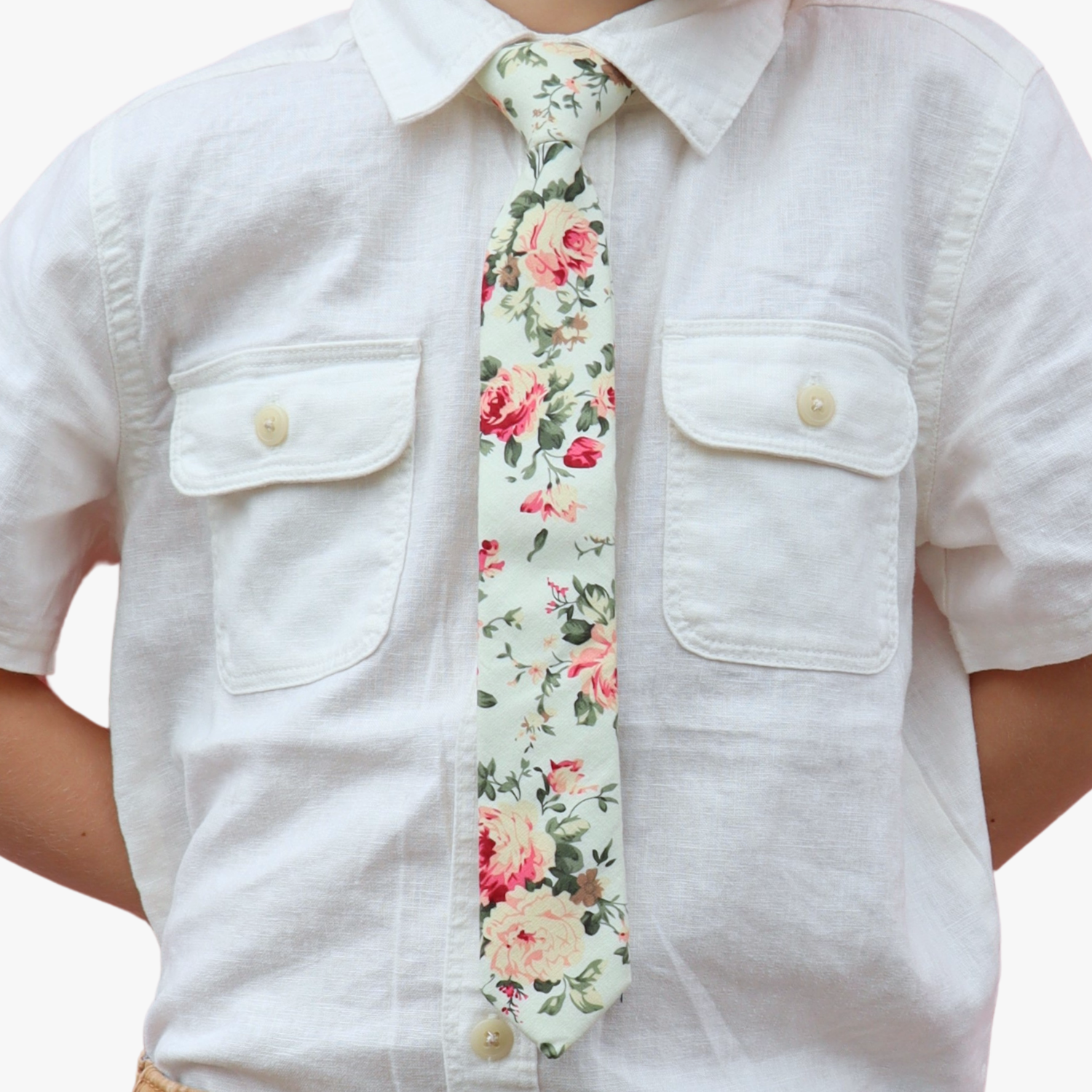 The torso of a boy wearing a floral kids tie with pink rose flowers, yellow petals, dark blossoms and green leaves.