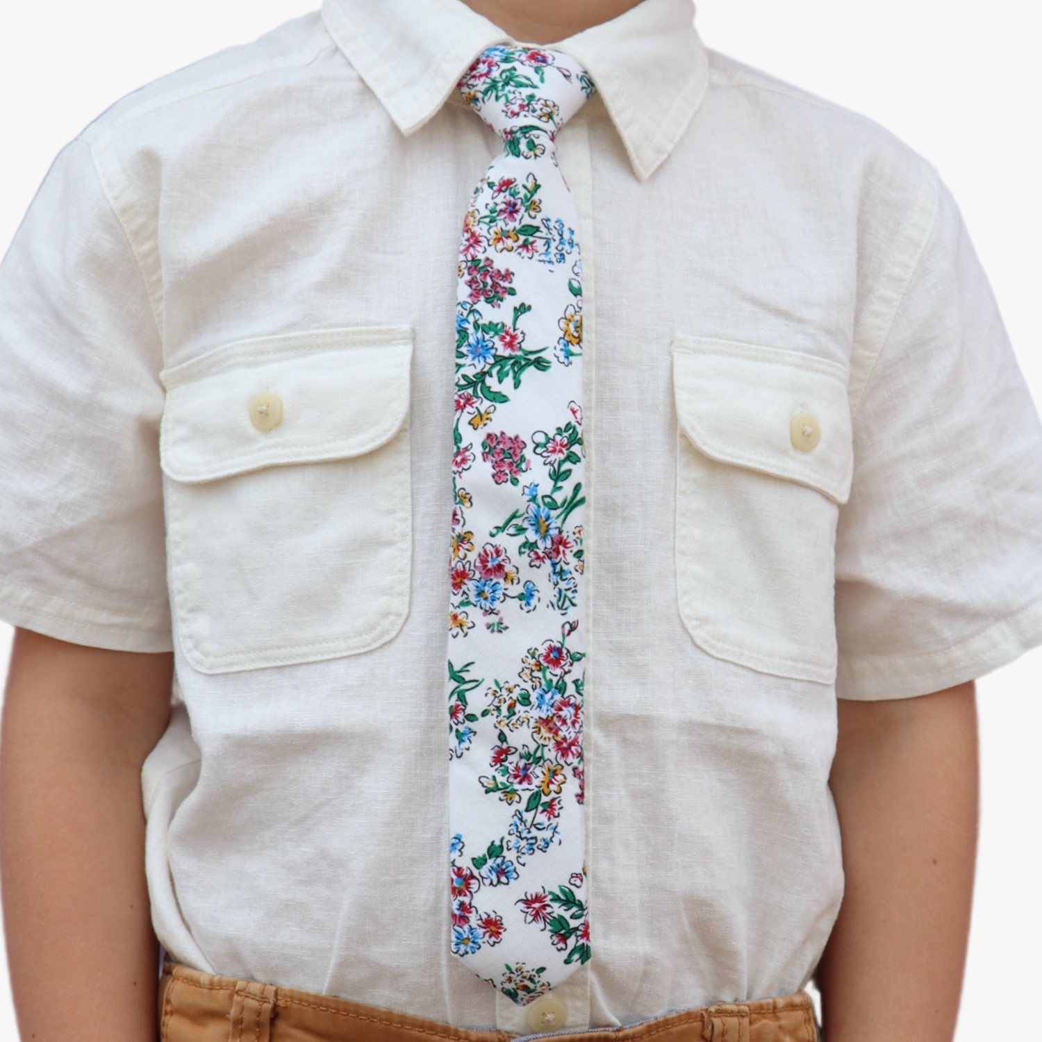 The torso of a boy wearing a floral kids tie with watercolor turquoise flowers, pink and yellow blossoms, and green leaves.