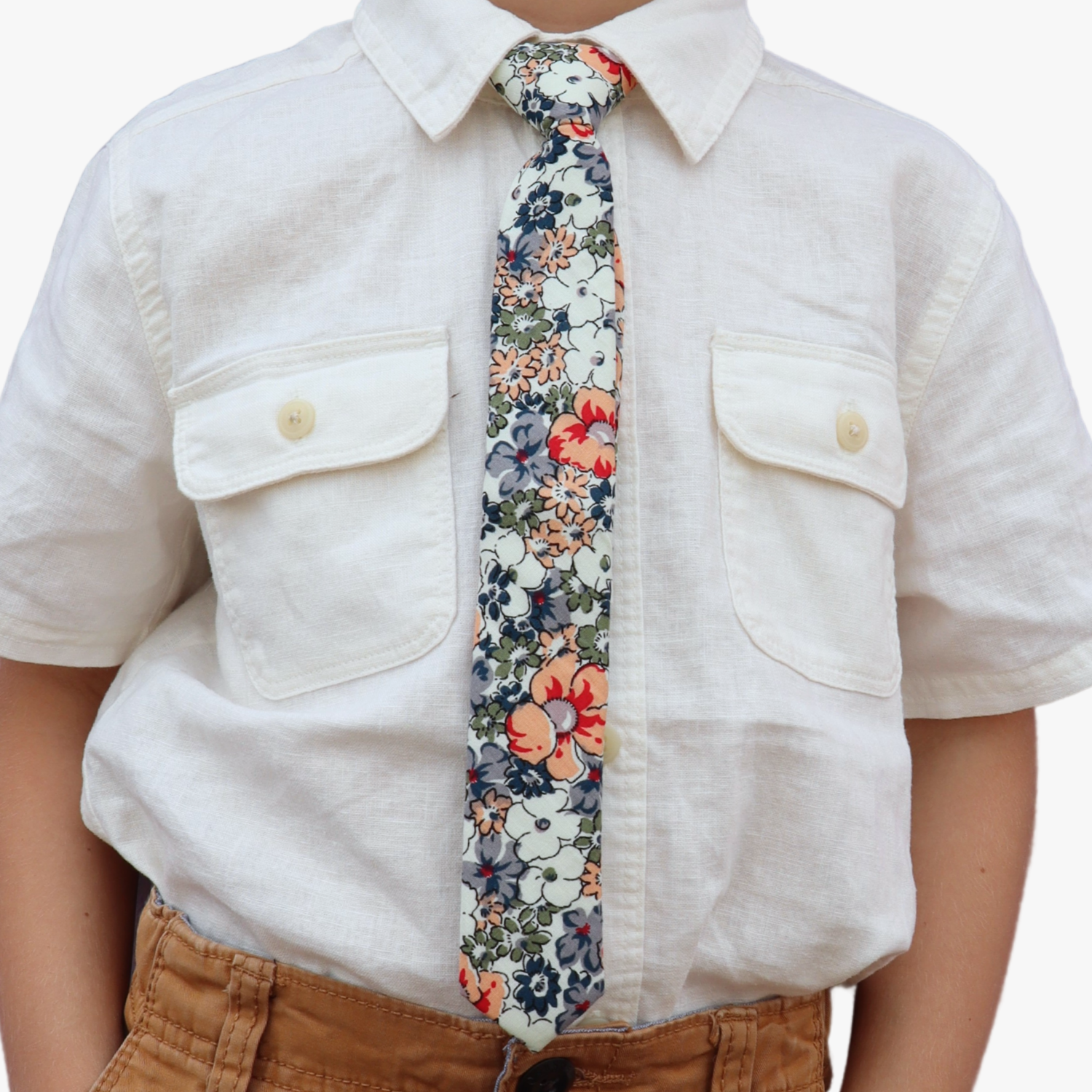 The torso of a boy wearing a floral kids tie with blue flowers, white petals, and peach or salmon blossoms and green leaves.
