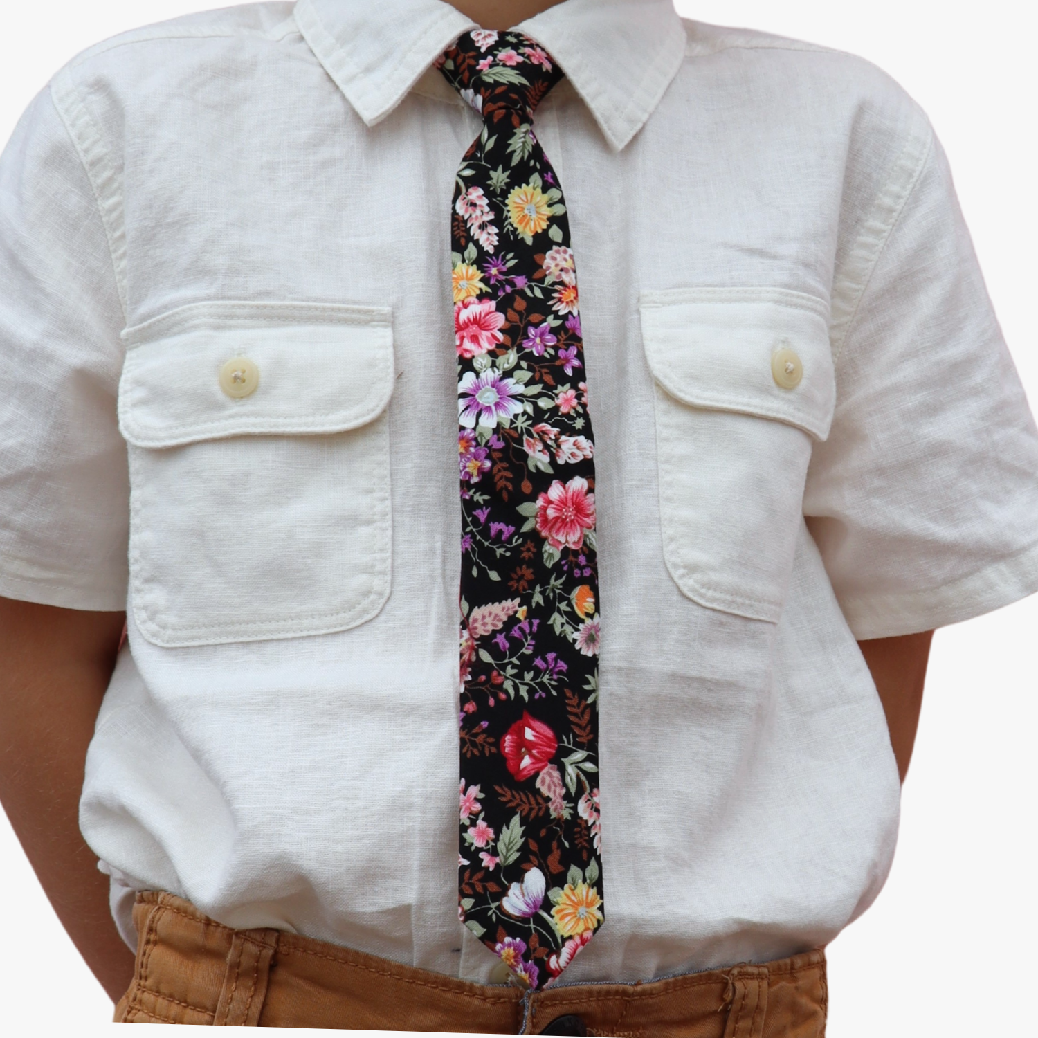 The torso of a boy wearing a floral kids tie with pink flowers, yellow petals, wisteria purple blossoms and brown leaves.