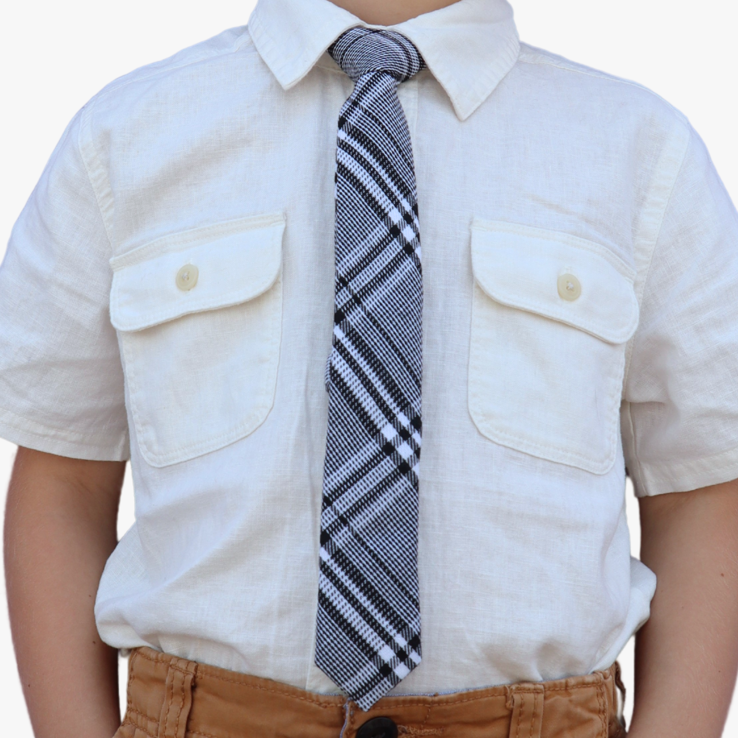 The torso of a boy wearing a plaid kids tie with black plaid pattern with light gray stripes, and diagonal white bars.