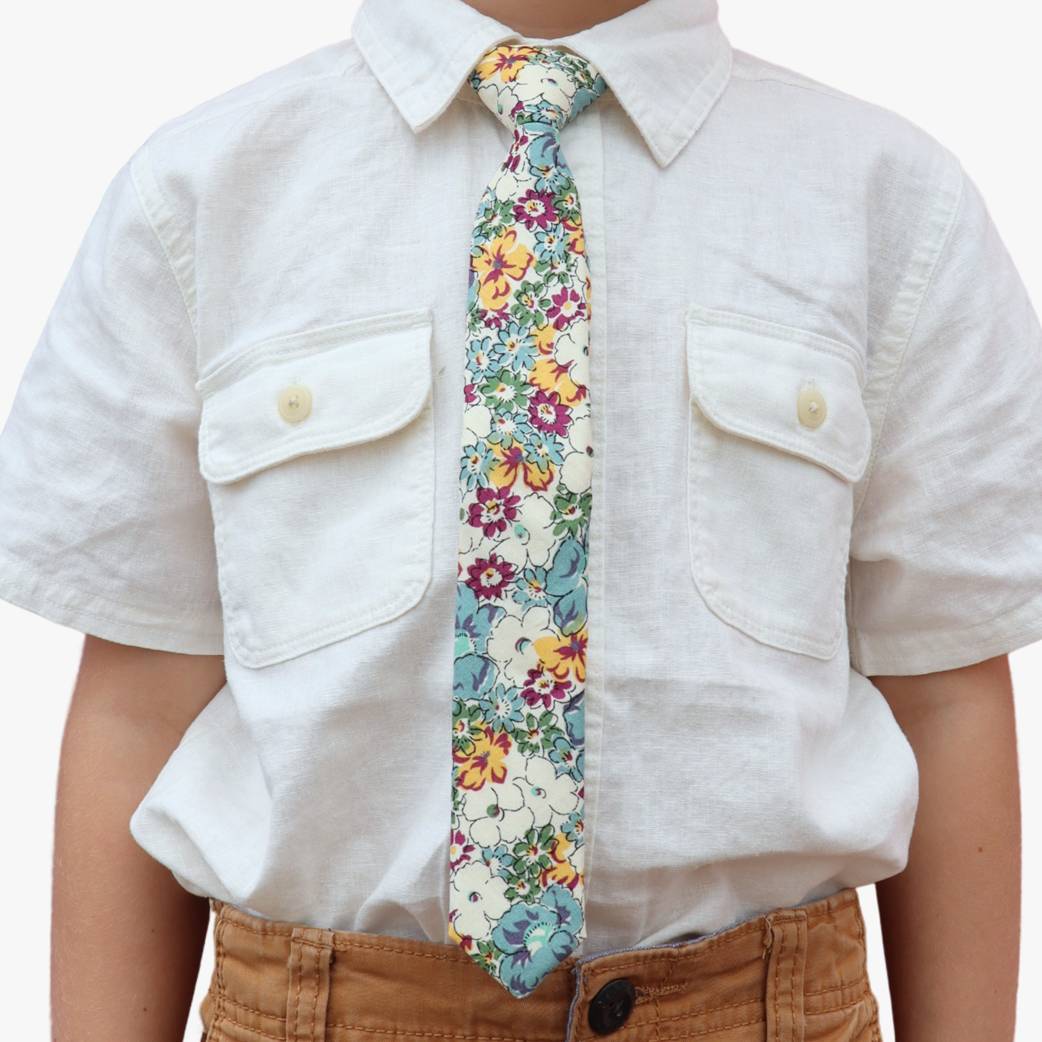 The torso of a boy wearing a floral kids tie with blue flowers, yellow and orange petals, white blossoms and green accents.