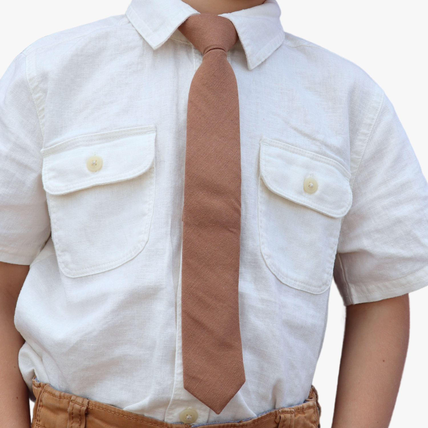 The torso of a boy wearing a solid kids tie with plain light chocolate taupe brown color.