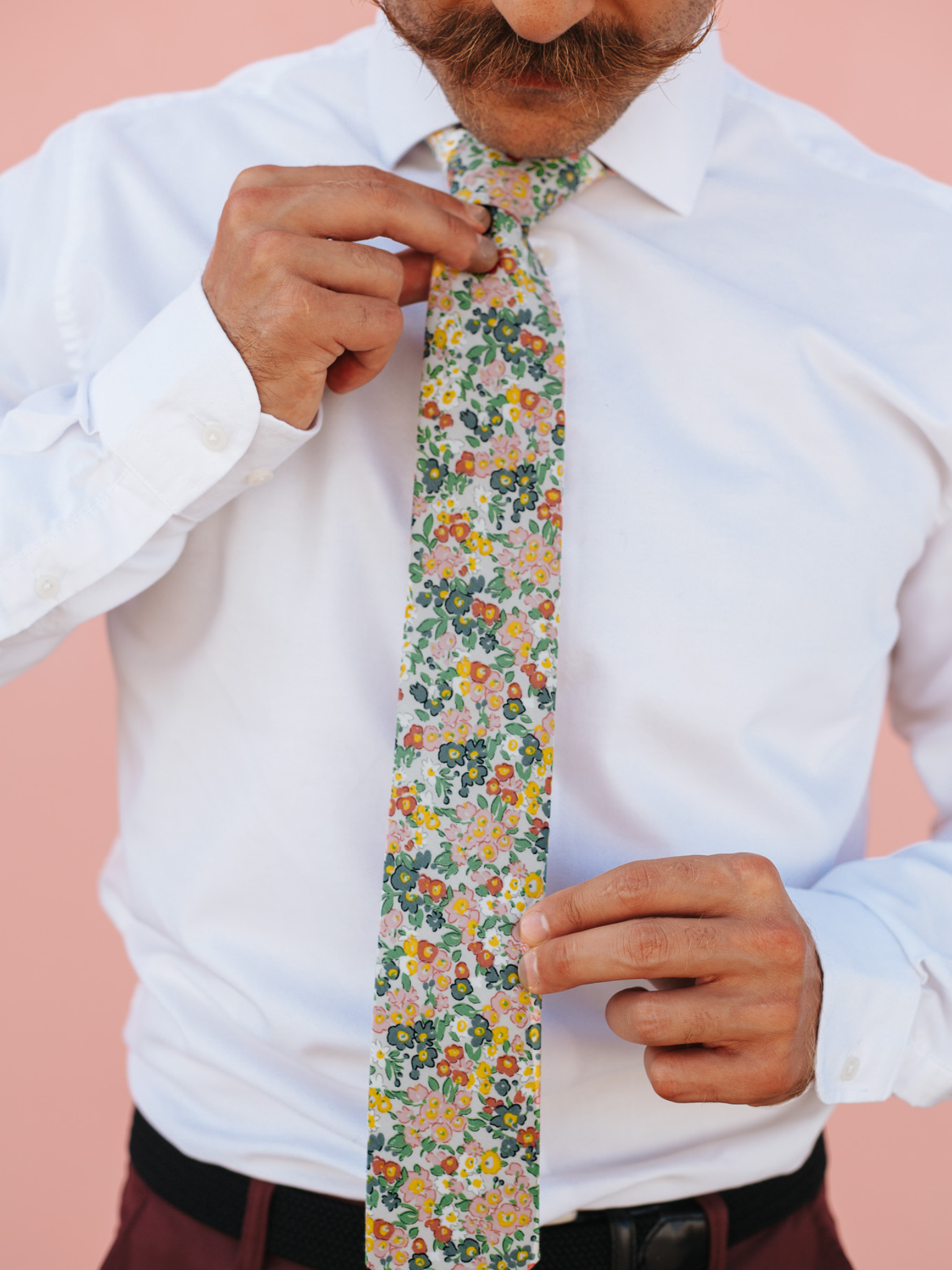 A close up of a man wearing a white and pink flower cotton skinny tie for weddings, grooms, and groomsmen.