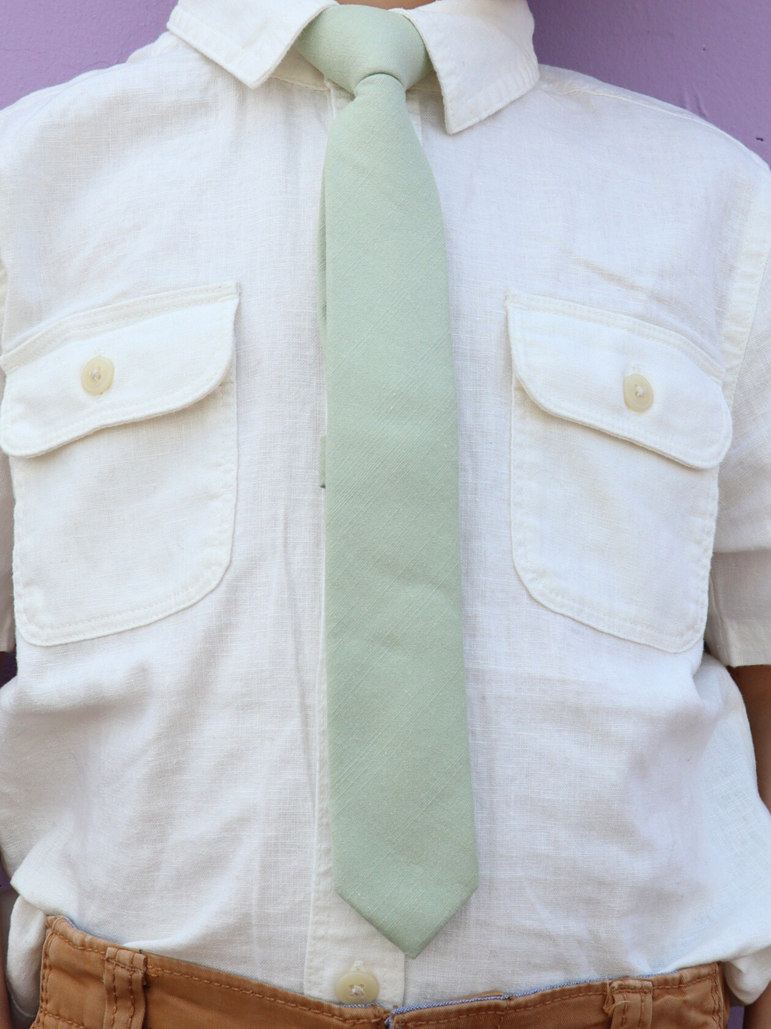 The torso of a boy wearing a solid kids tie with plain neutral sage green color.