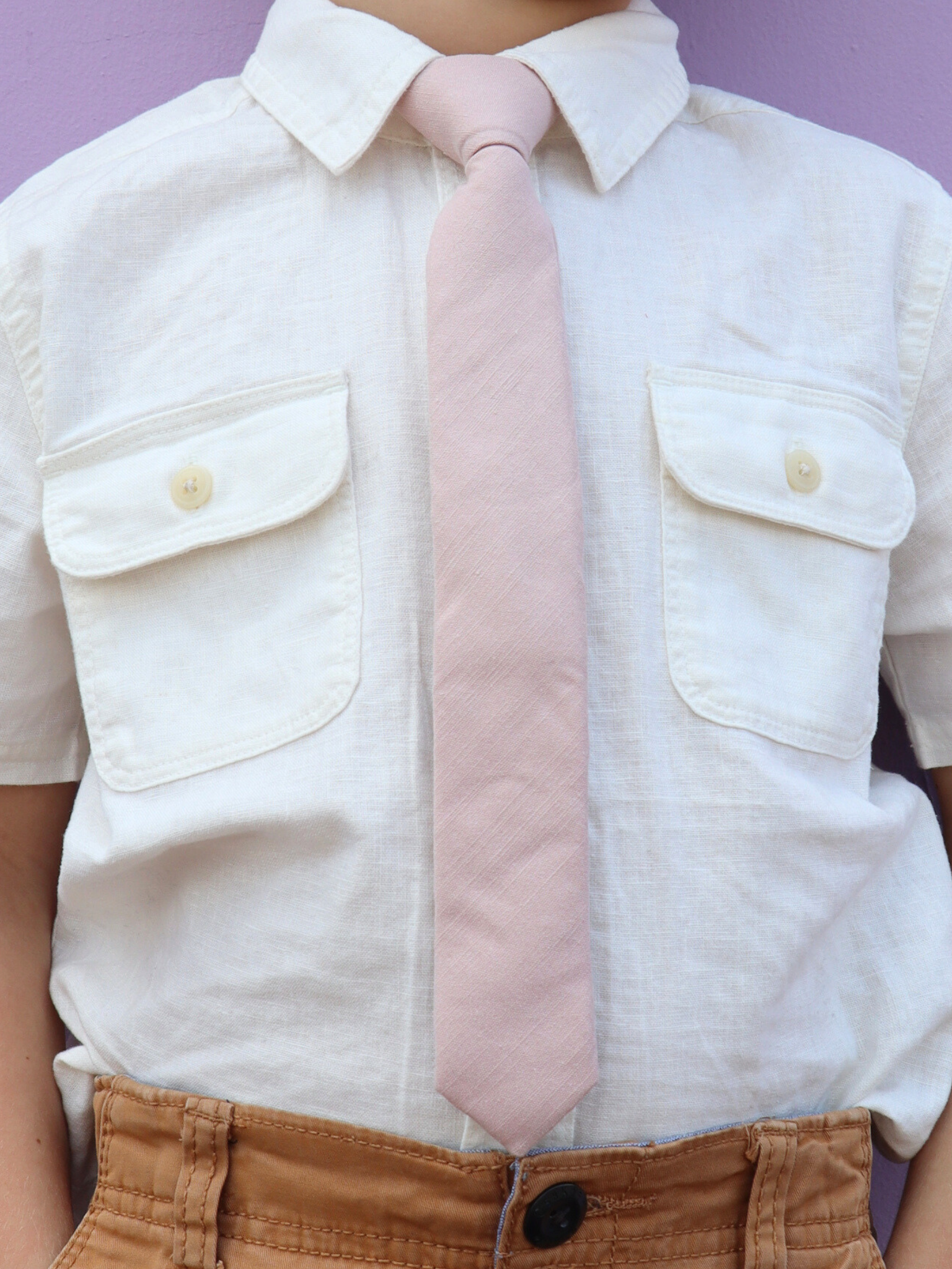 The torso of a boy wearing a solid kids tie with plain neutral pink taupe color.