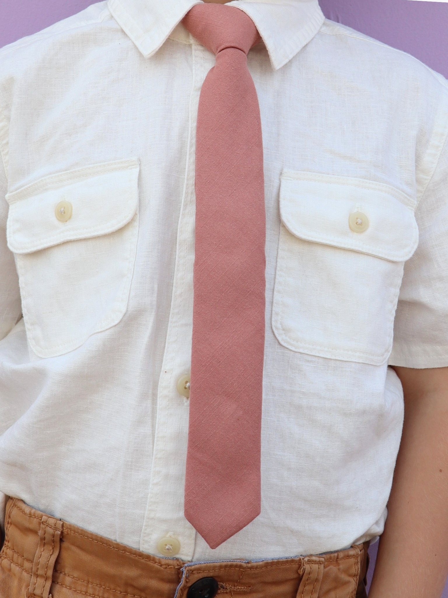 The torso of a boy wearing a solid kids tie with plain rosewood rosegold light pink color.