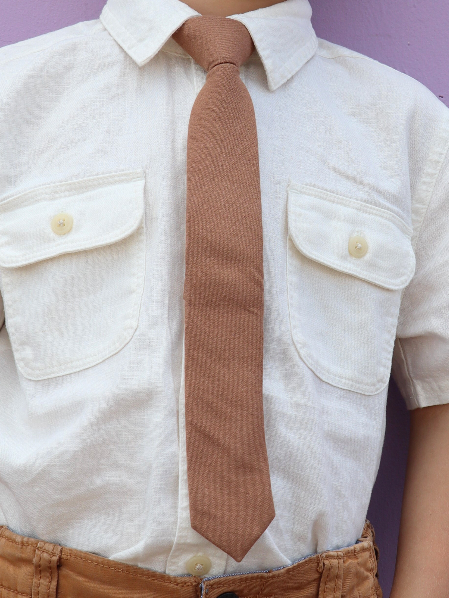 The torso of a boy wearing a solid kids tie with plain light chocolate taupe brown color.