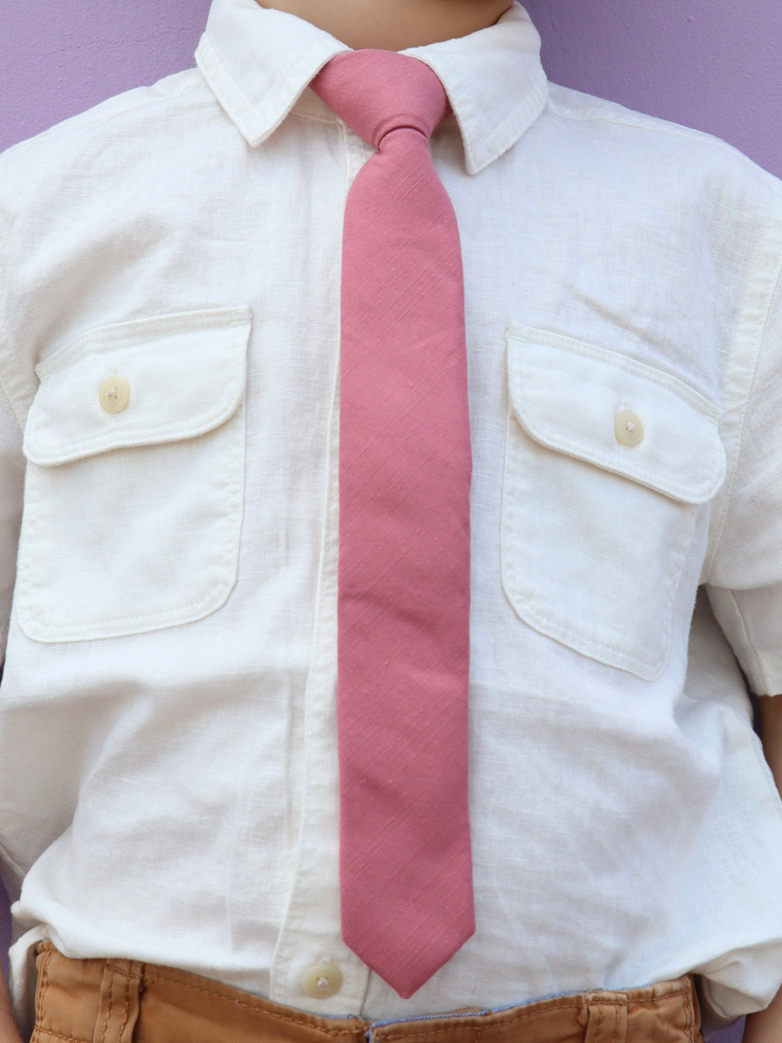 The torso of a boy wearing a solid kids tie with plain darker rose-gold dusty pink color.