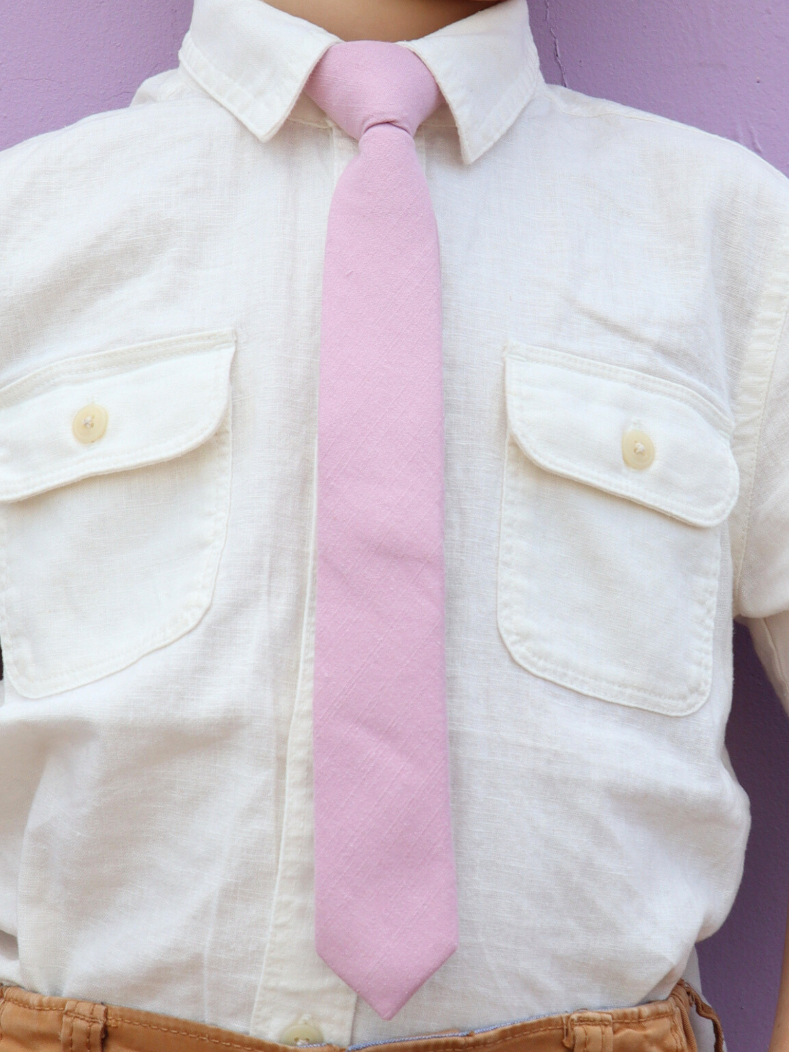 The torso of a boy wearing a solid kids tie with plain light rose dusty pink color.