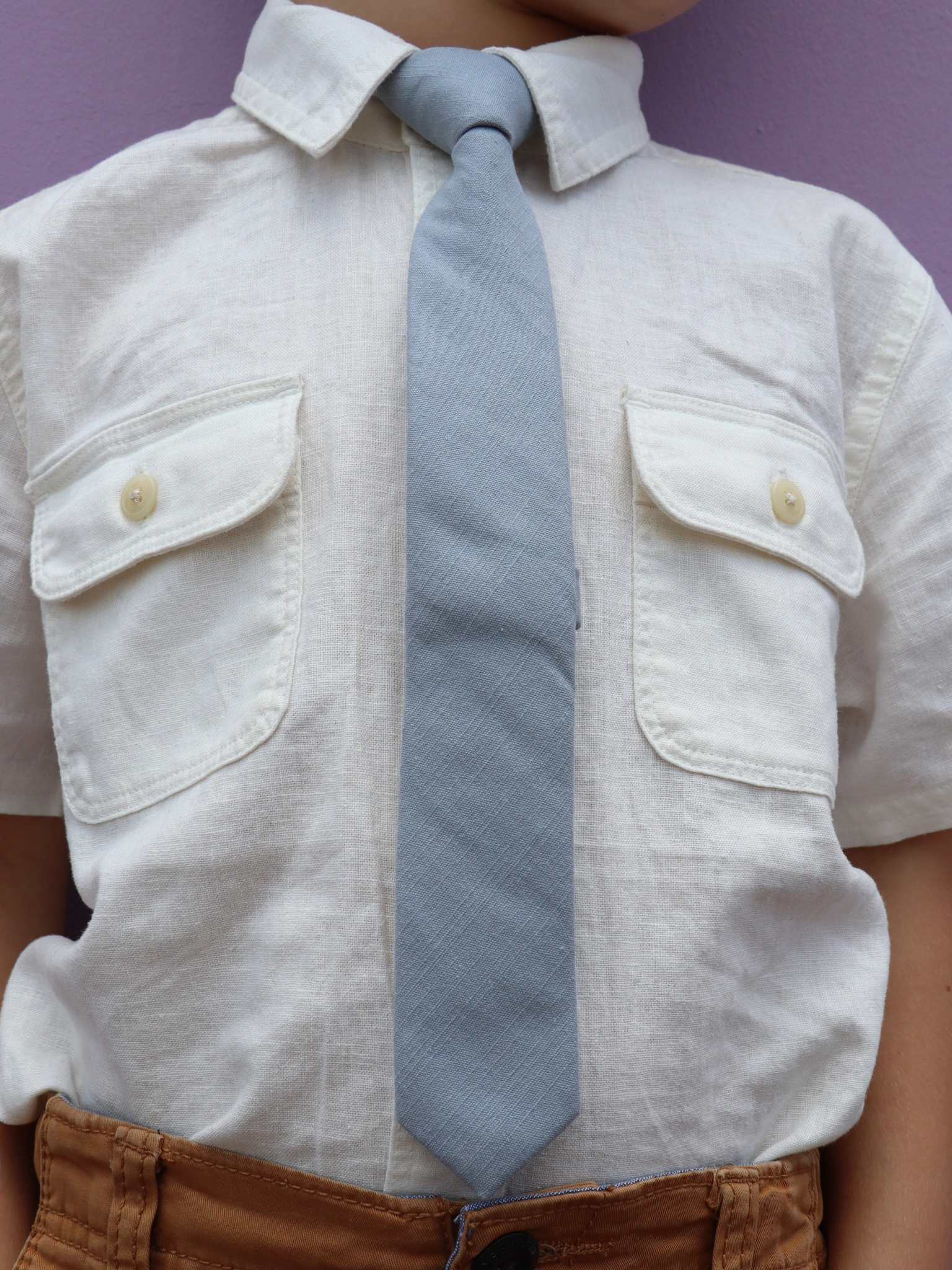 The torso of a boy wearing a solid kids tie with plain pale solid blue/gray color.