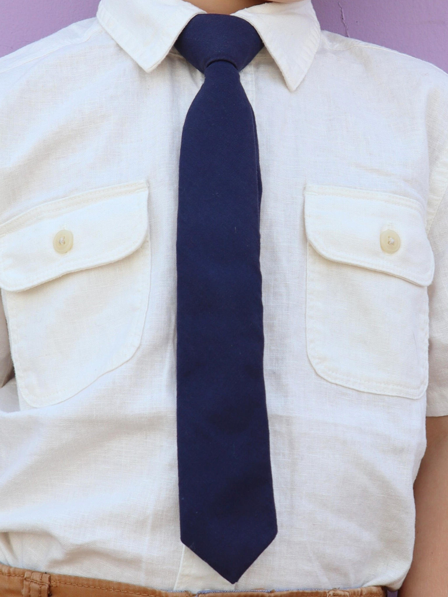 The torso of a boy wearing a solid kids tie with plain navy blue color.