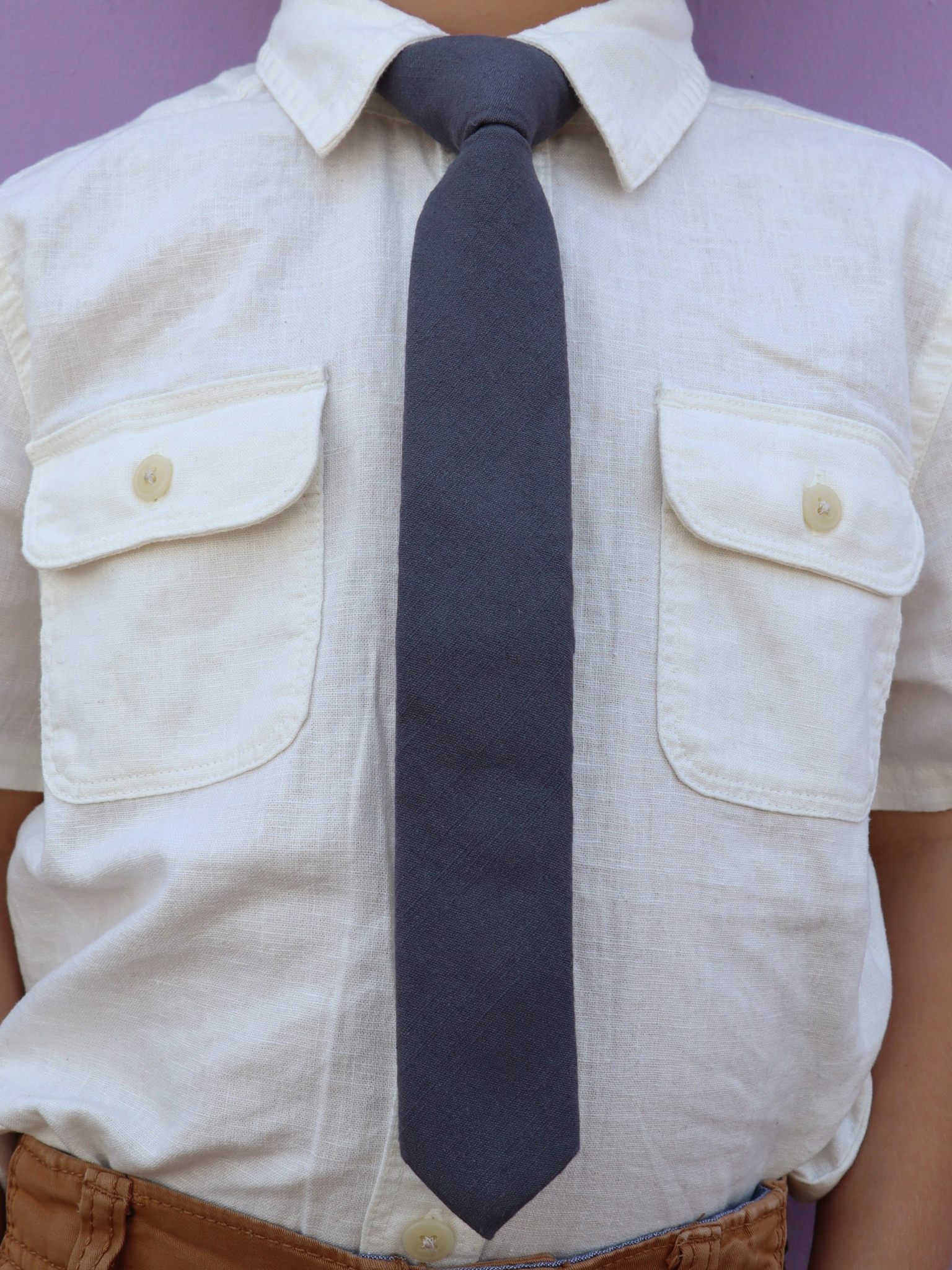 The torso of a boy wearing a solid kids tie with plain dark gray/grey color.