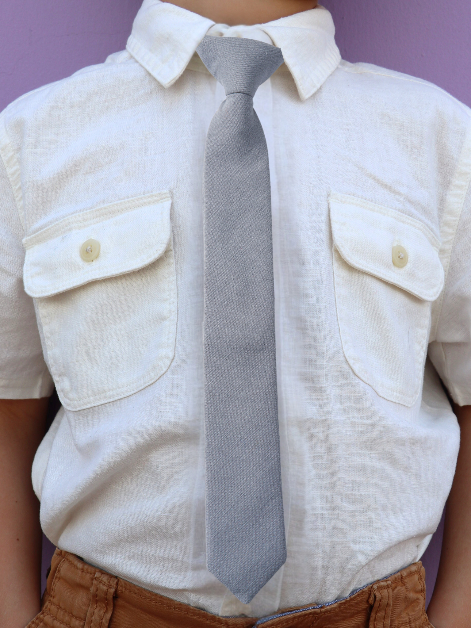 The torso of a boy wearing a solid kids tie with plain neutral light gray-blue color.