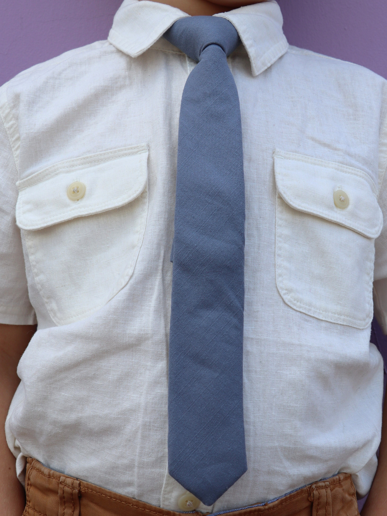 The torso of a boy wearing a solid kids tie with plain deep cobalt blue color.