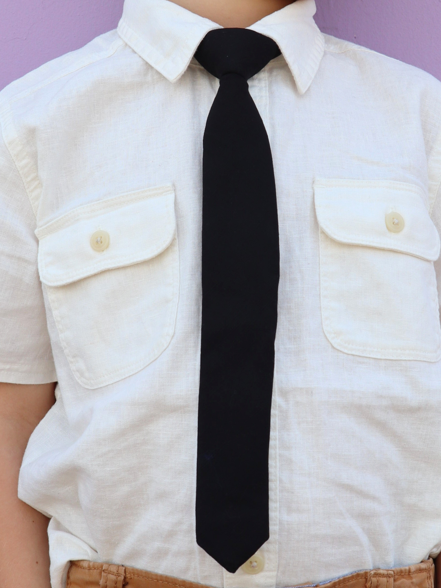 The torso of a boy wearing a solid kids tie with plain pitch black color.