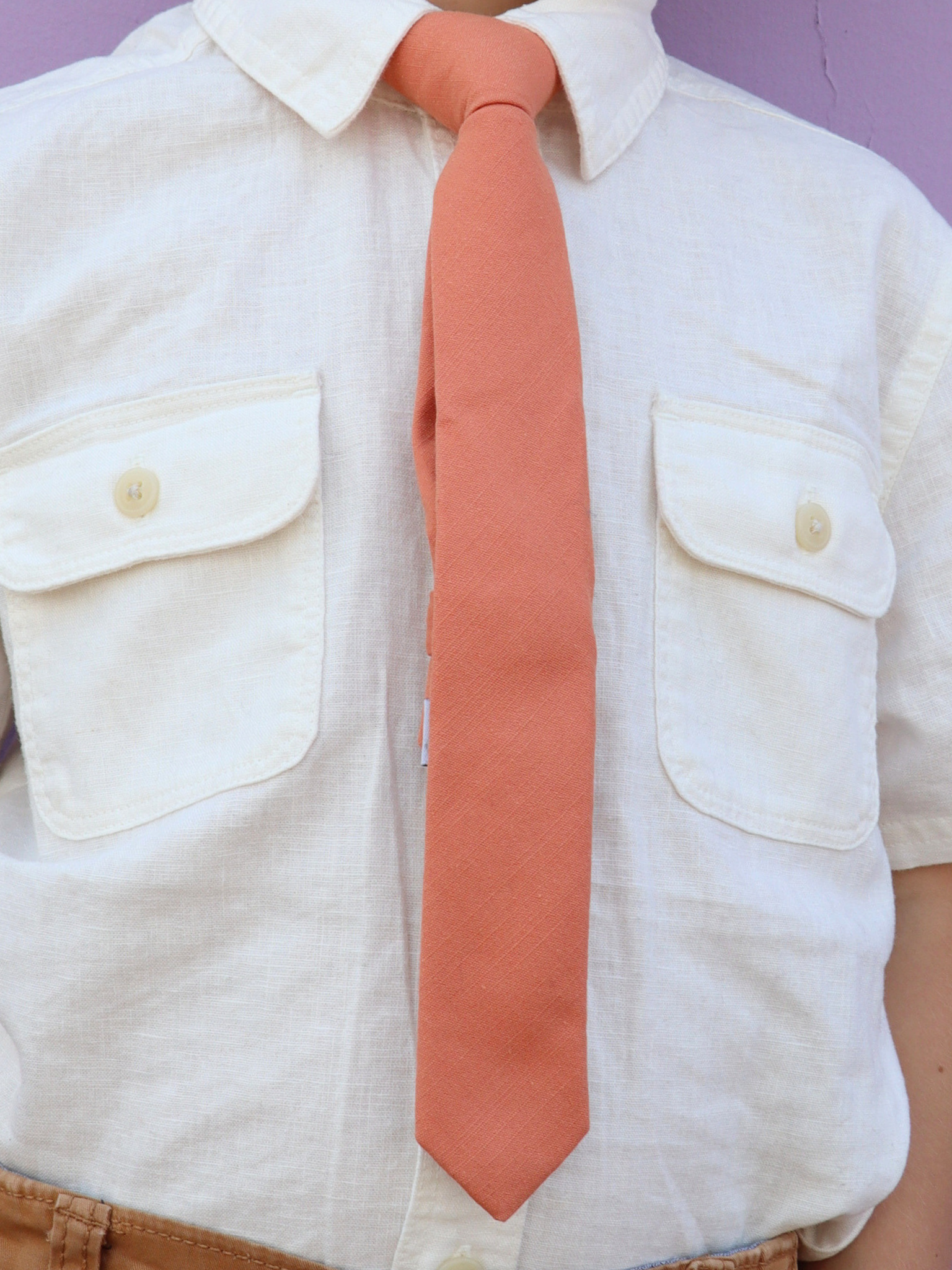 The torso of a boy wearing a solid kids tie with plain burnt orange salmon color.