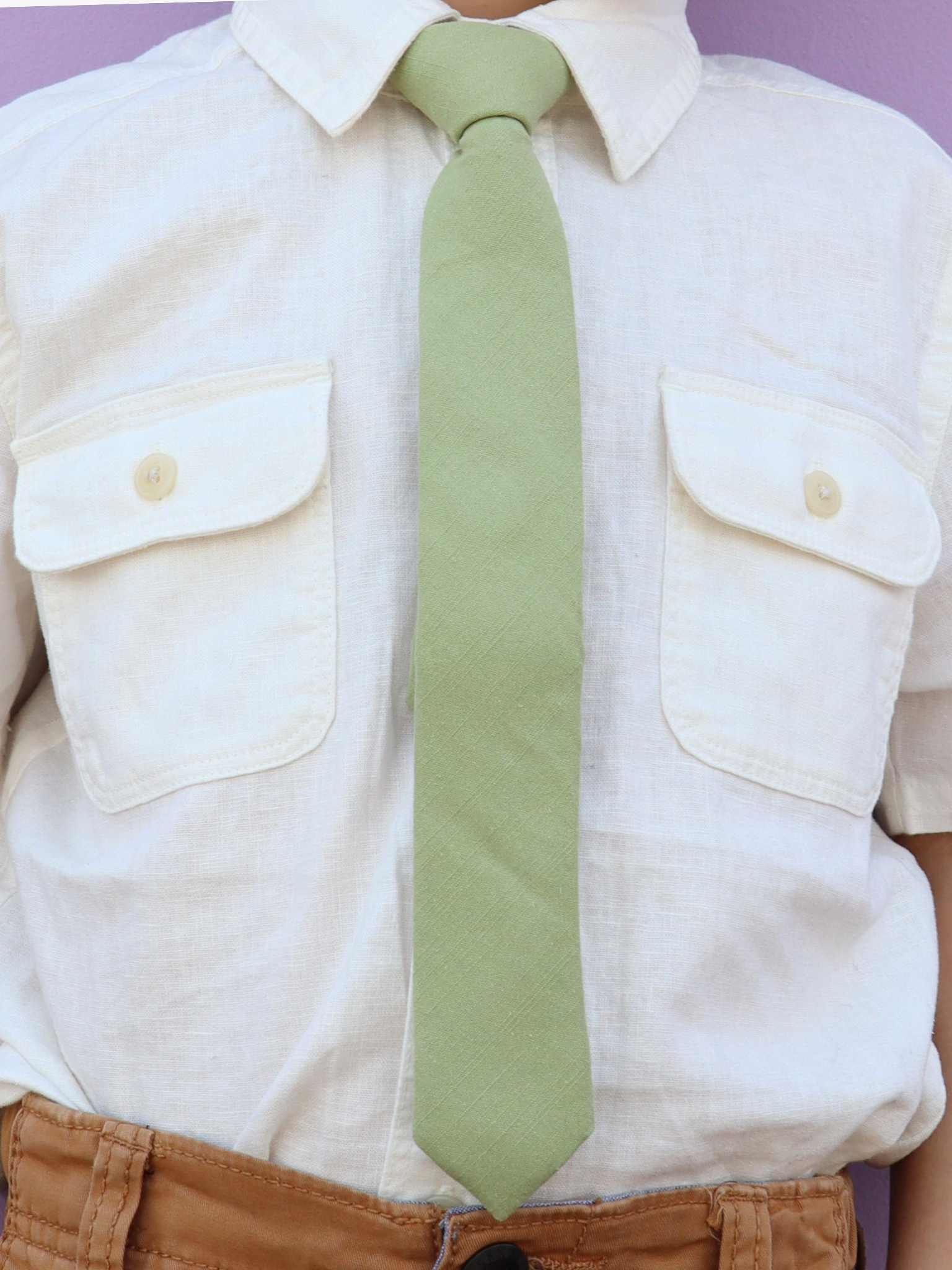 The torso of a boy wearing a solid kids tie with plain neutral light green color.