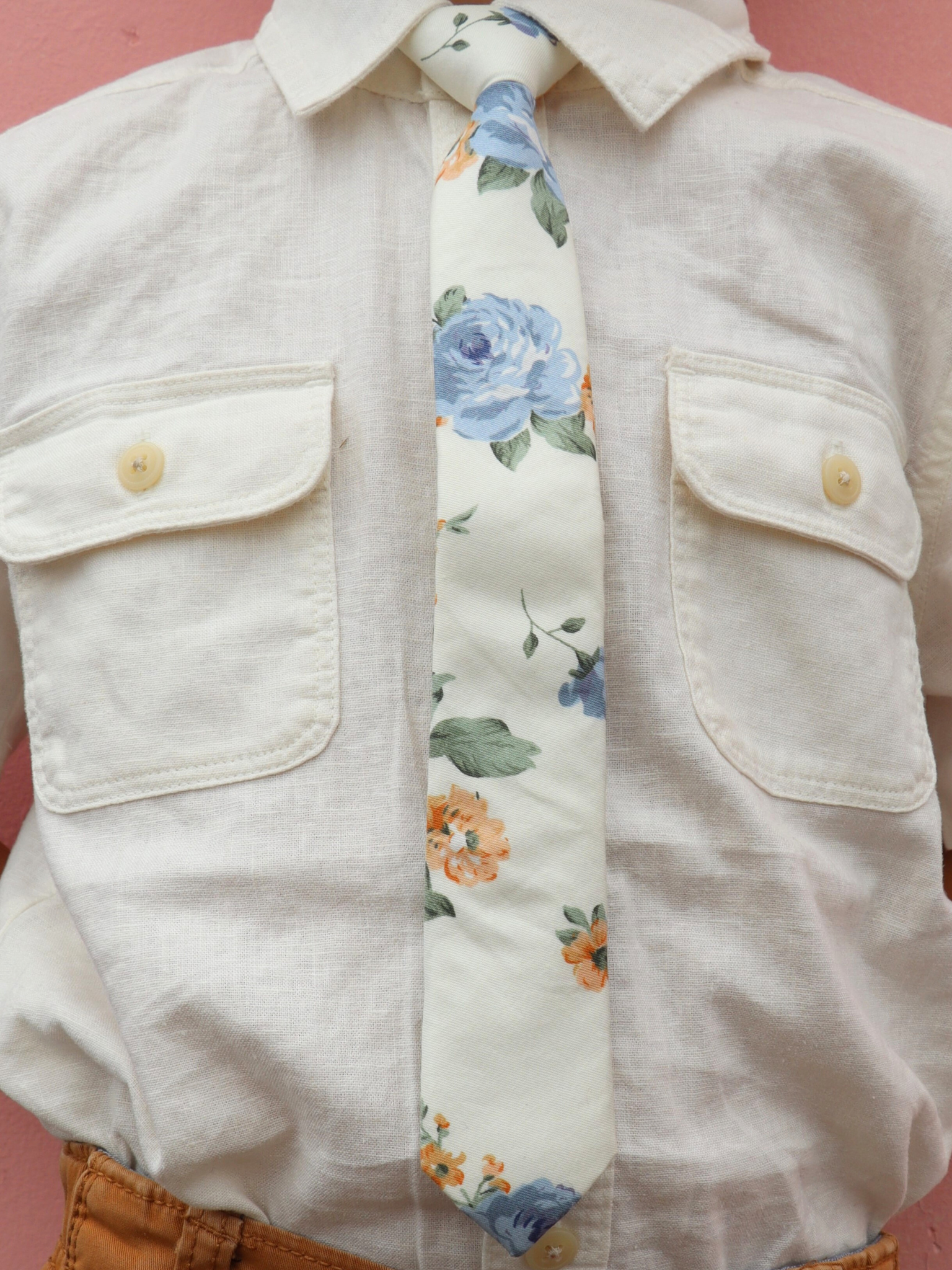 The torso of a boy wearing a floral kids tie with dusty blue rose flowers, deep yellow petals, and light green leaves.