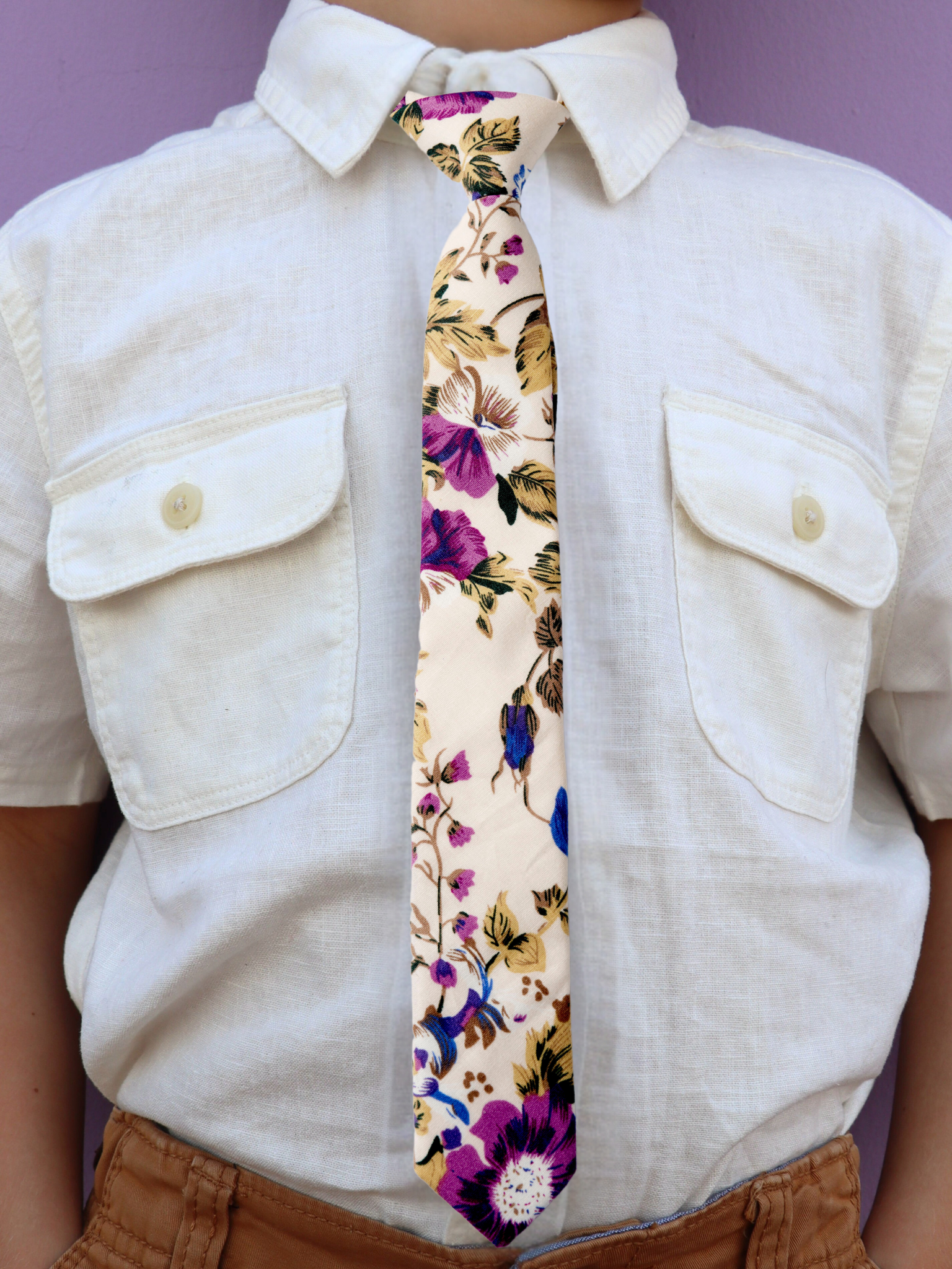 The torso of a boy wearing a floral kids tie with purple flowers, blue petals, brown accents and fall leaves.