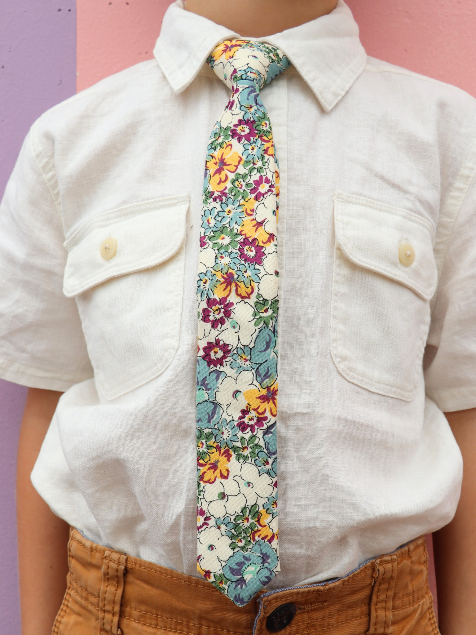 The torso of a boy wearing a floral kids tie with blue flowers, yellow and orange petals, white blossoms and green accents.