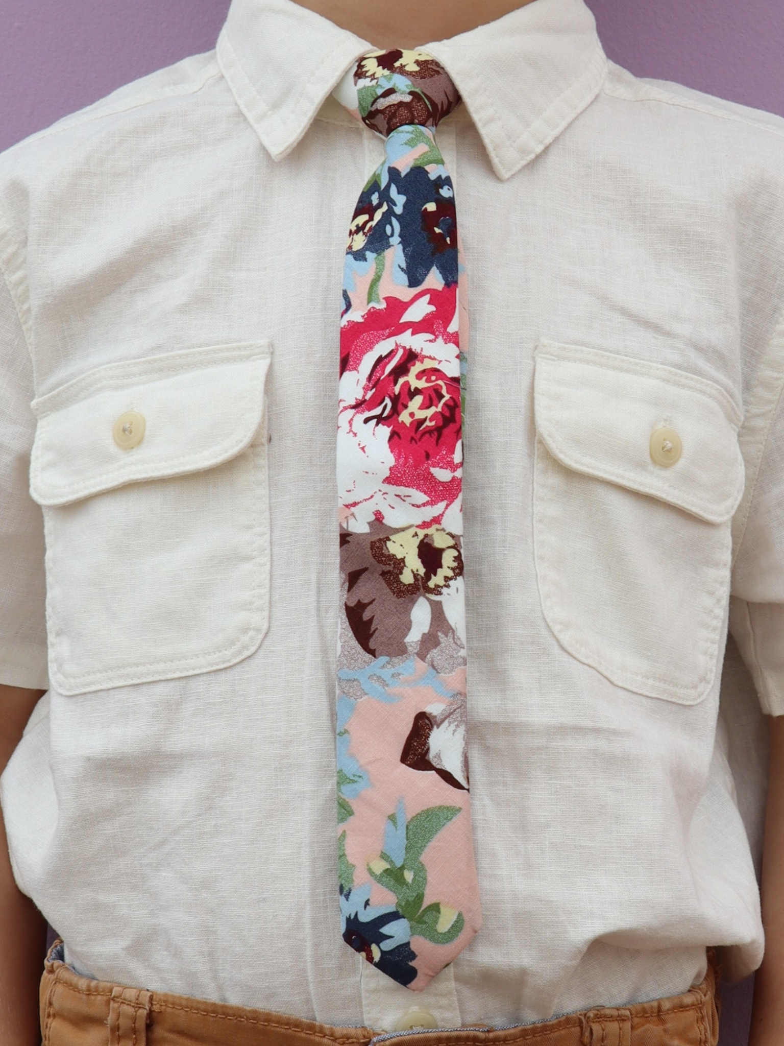 The torso of a boy wearing a floral kids tie with dark blue flowers, brown petals, and light green water leaves.