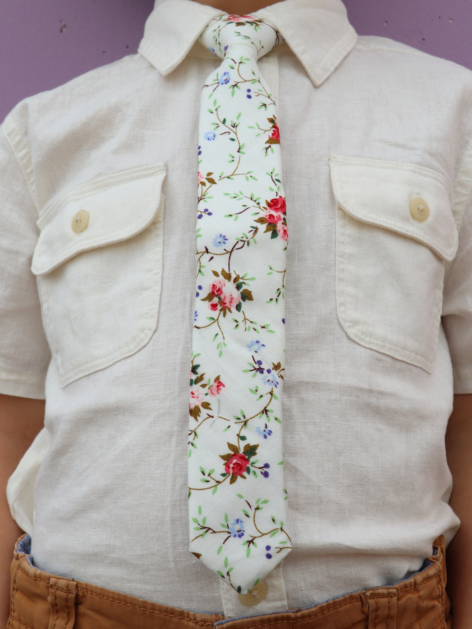 The torso of a boy wearing a floral kids tie with red flowers, pink petals, Christmas blossoms and green leaves.