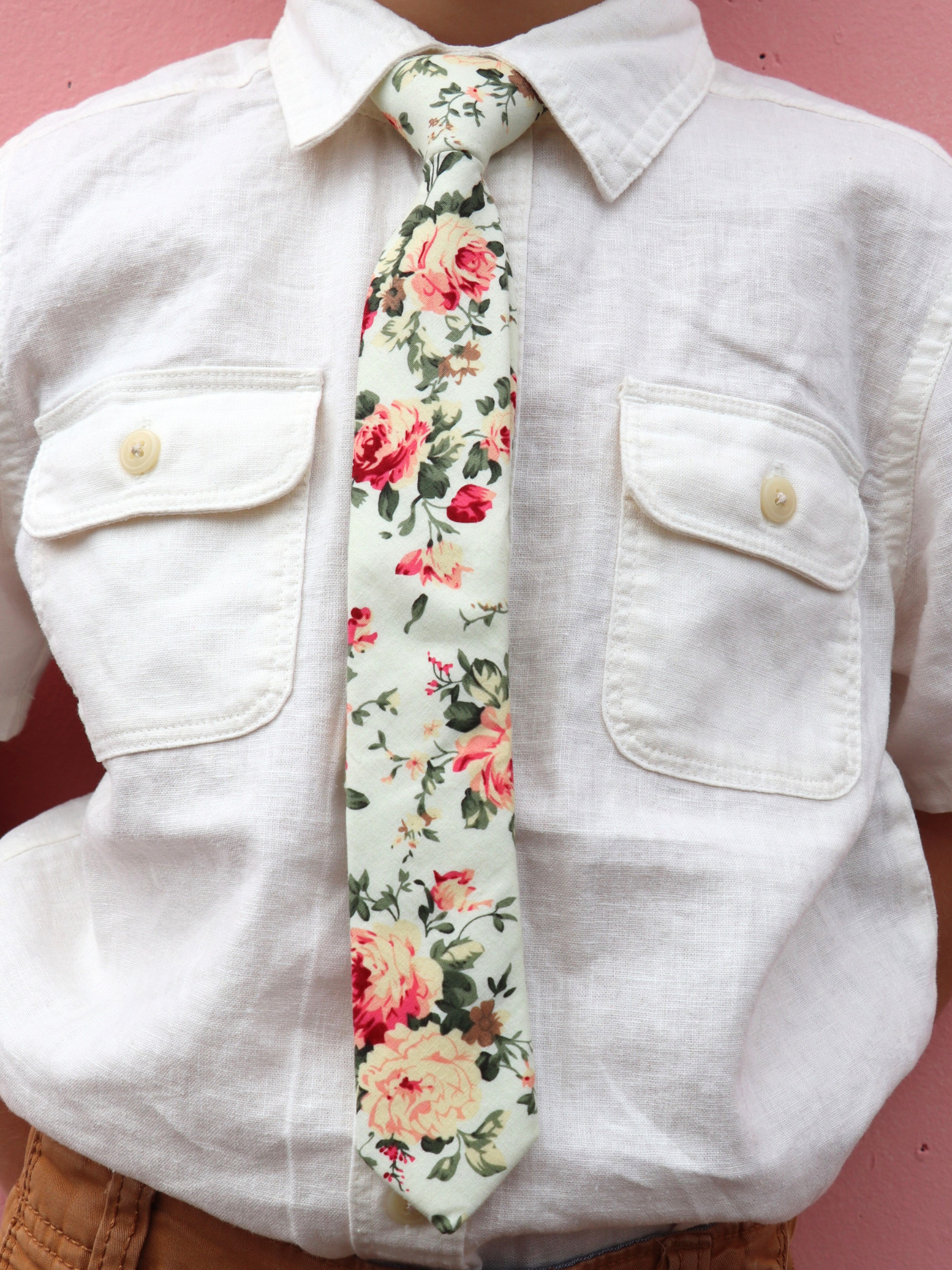 The torso of a boy wearing a floral kids tie with pink rose flowers, yellow petals, dark blossoms and green leaves.