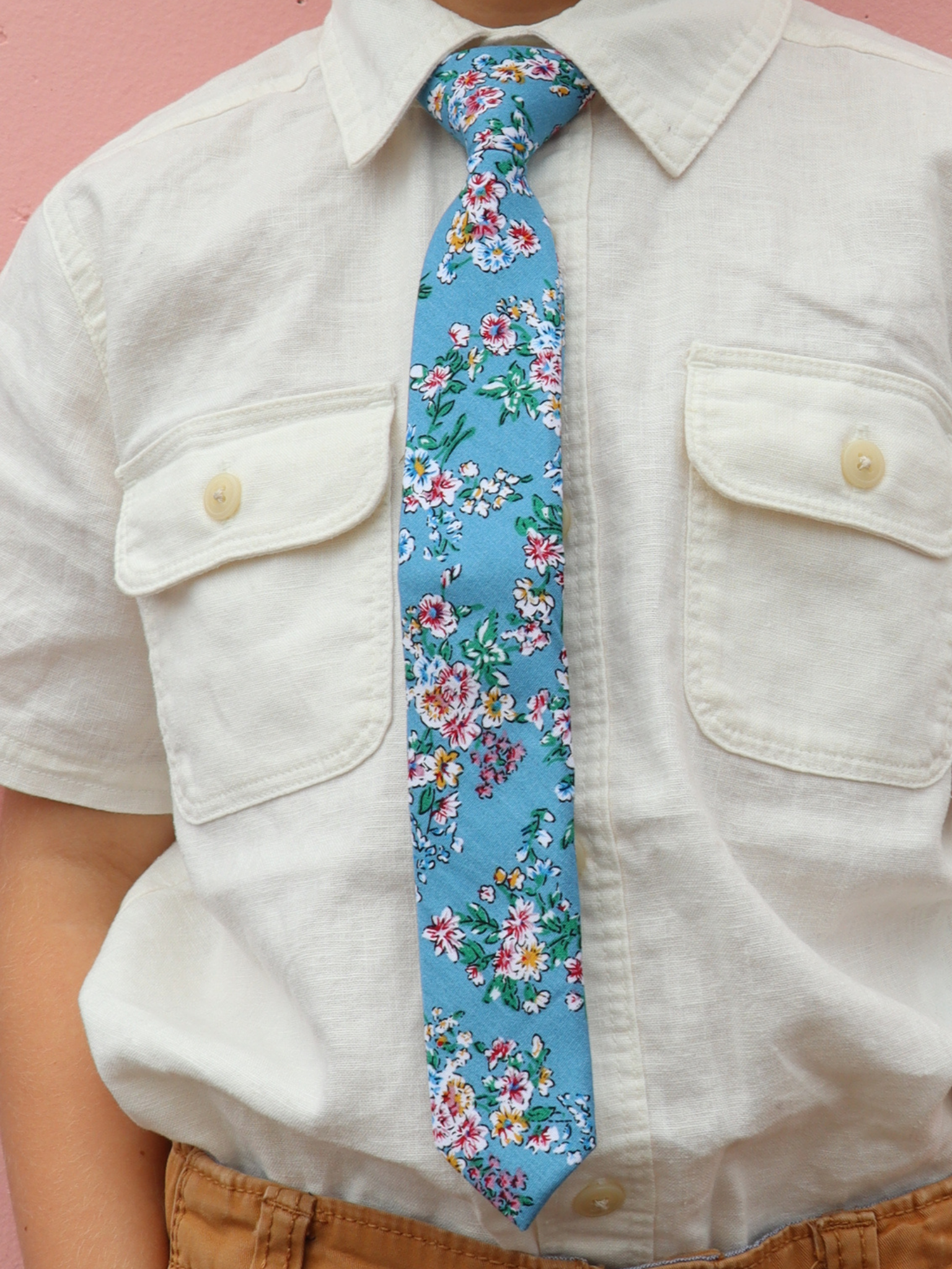 The torso of a boy wearing a floral kids tie with watercolor turqouise flowers, pink and yellow blossoms, and green leaves.