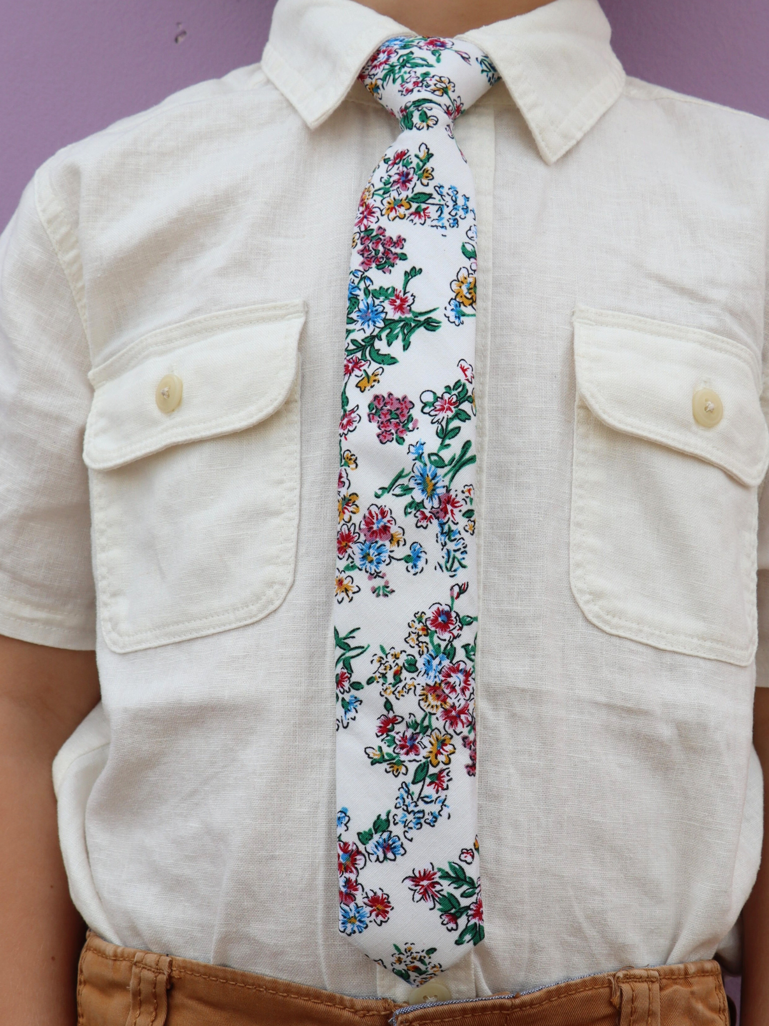 The torso of a boy wearing a floral kids tie with watercolor turquoise flowers, pink and yellow blossoms, and green leaves.