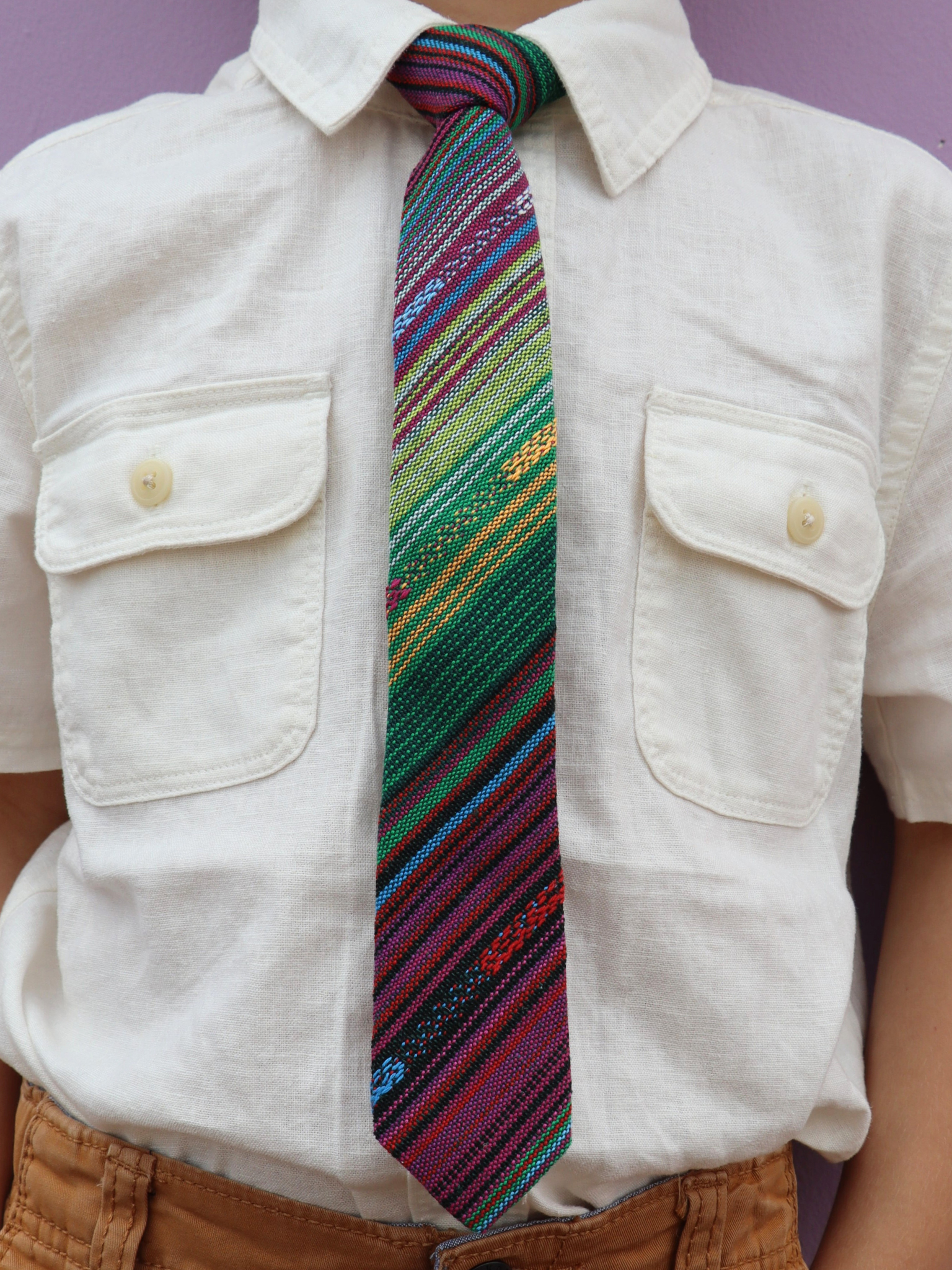 The torso of a boy wearing a striped kids tie with green stripes, purple lines, yellow bars, blue designs and Mexican styles.