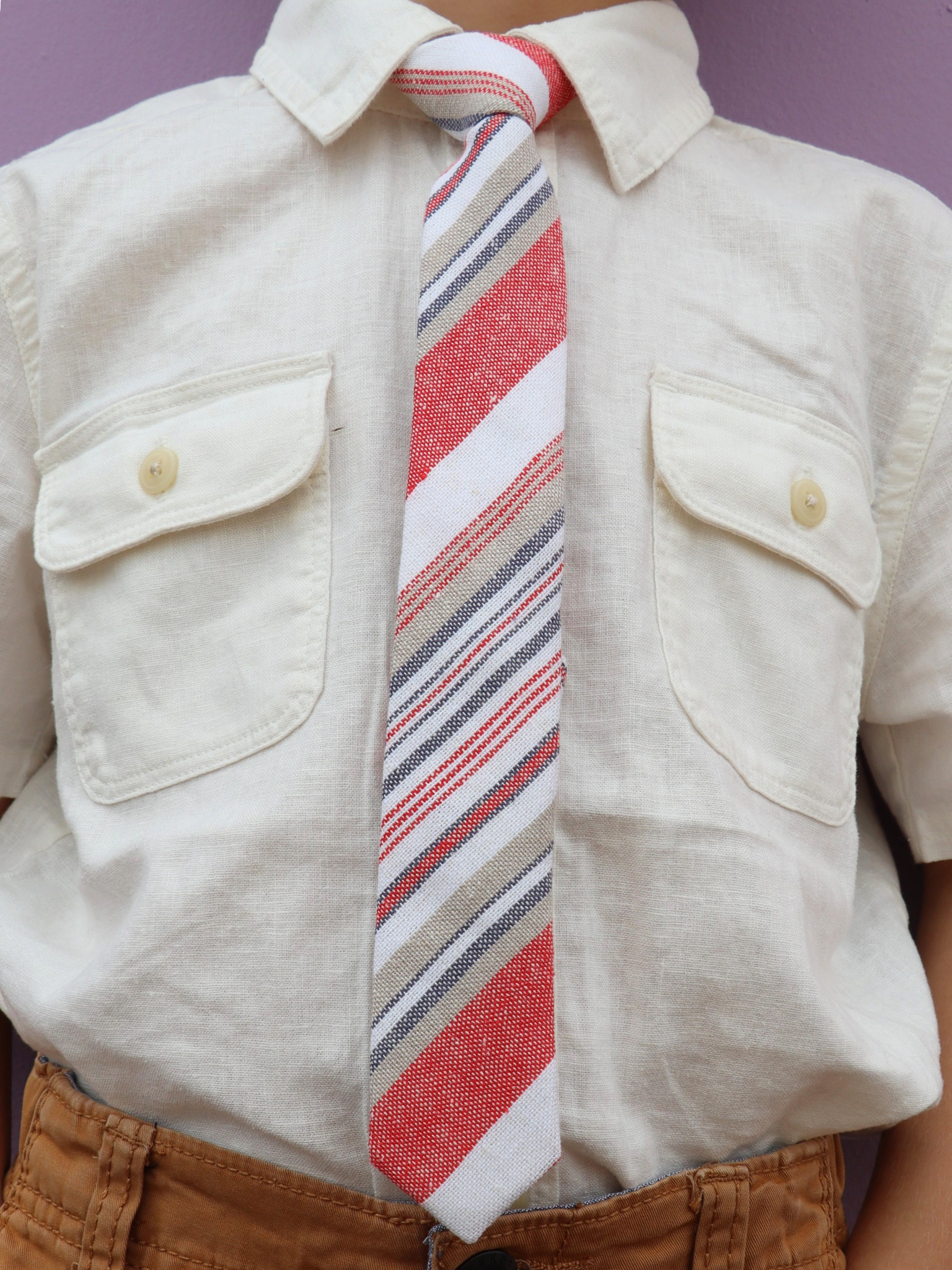 The torso of a boy wearing a striped kids tie with blood red stripes, white lines, gold bars and diagonal designs.