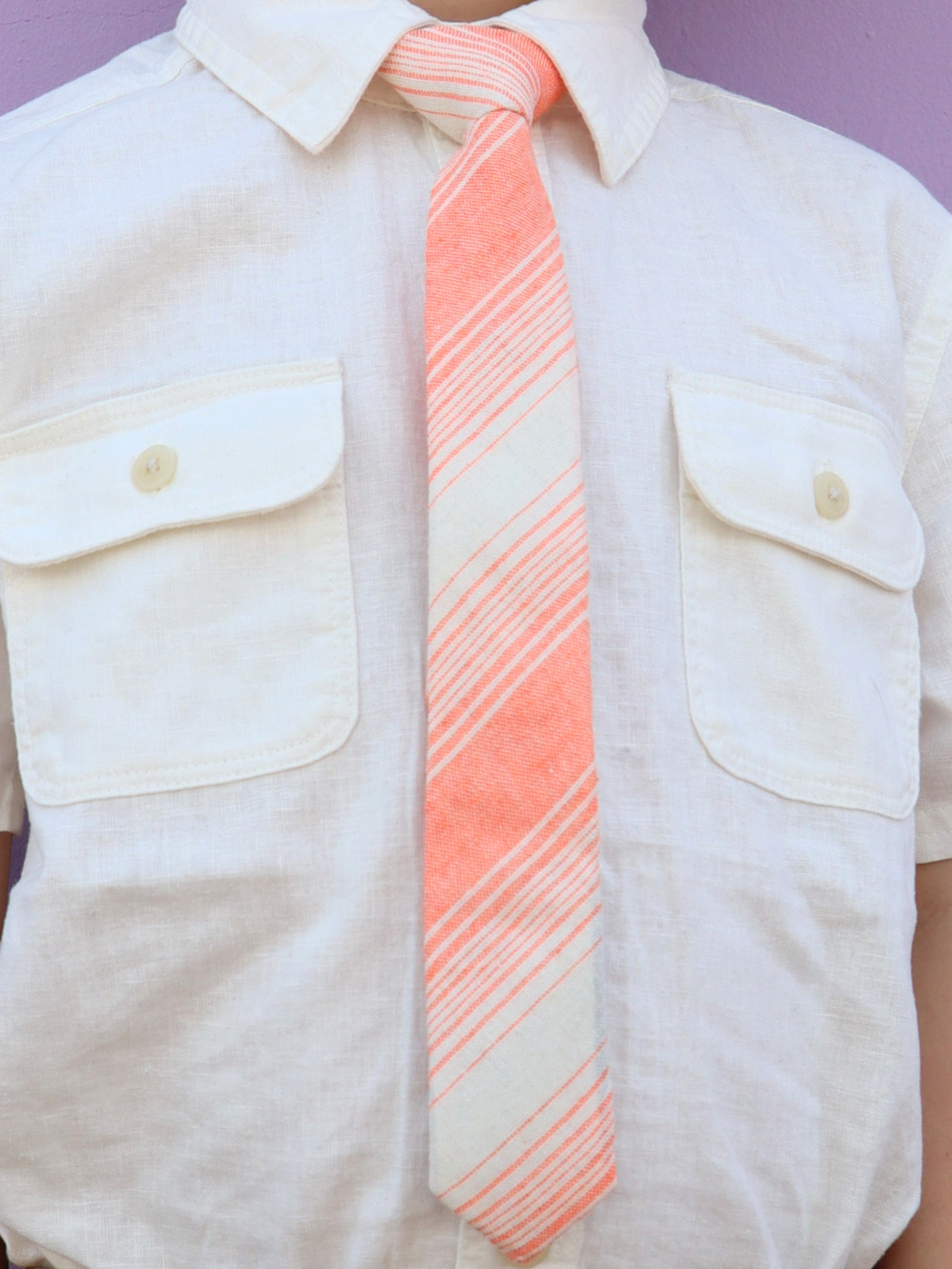 The torso of a boy wearing a striped kids tie with orange stripes, thin beige cream lines,  and off-white diagonal designs.