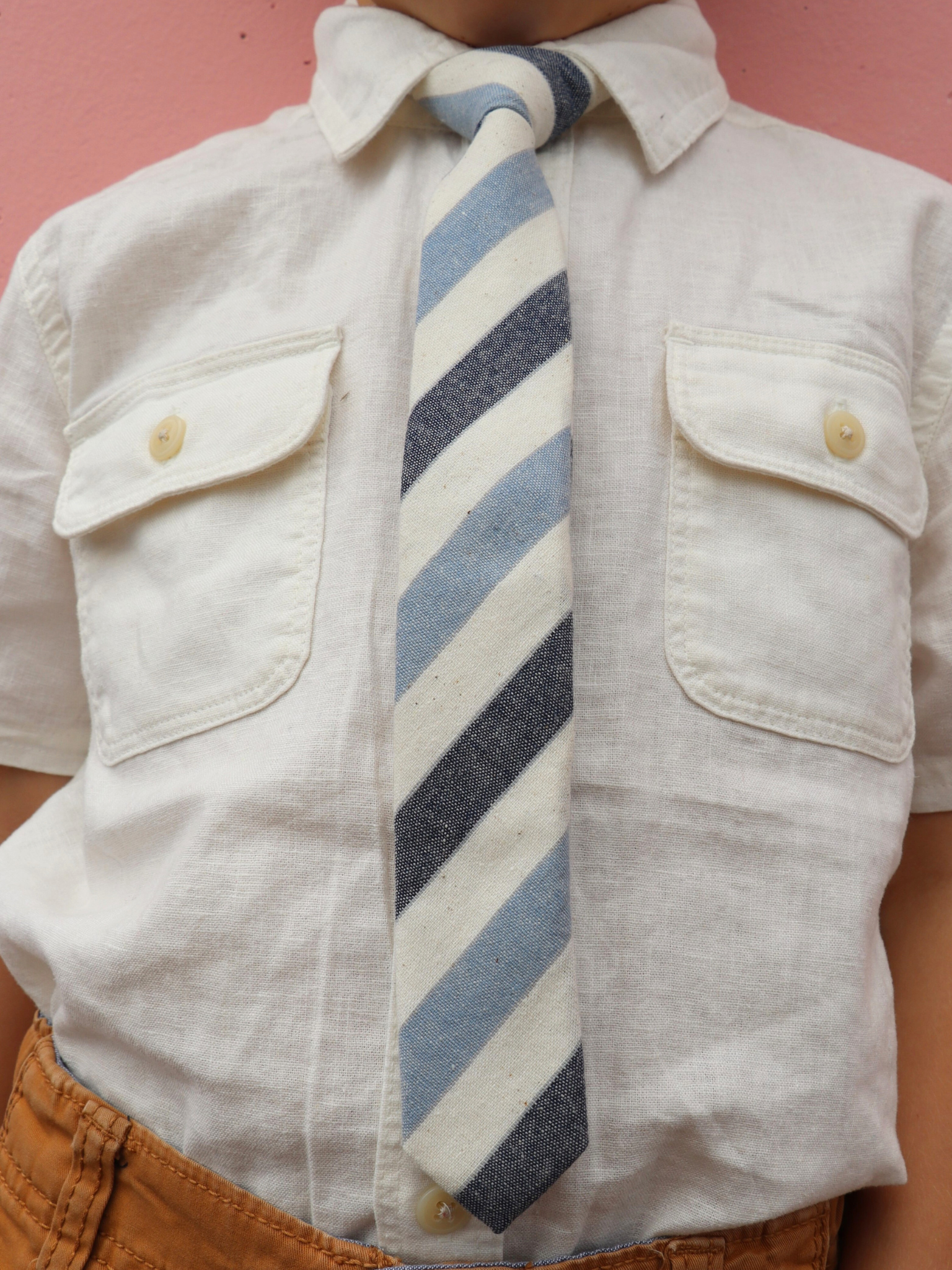 The torso of a boy wearing a striped kids tie with baby blue stripes, navy lines, cream bars, and off-white designs.