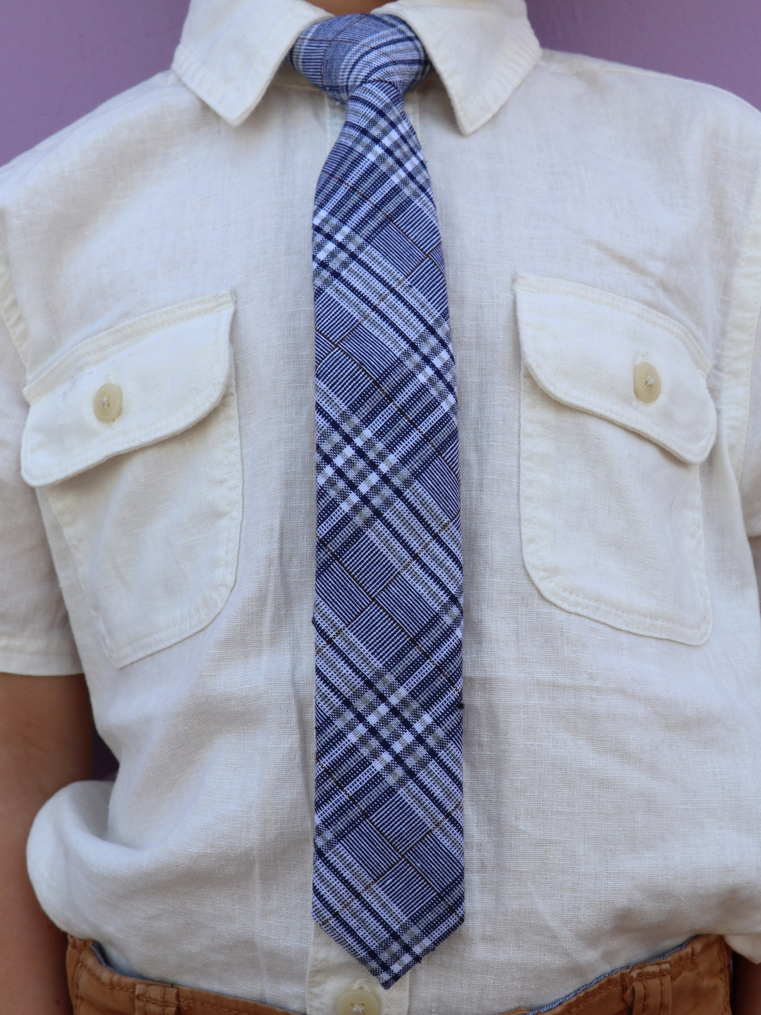 The torso of a boy wearing a plaid kids tie with navy plaid pattern with light blue stripes, and diagonal white bars.