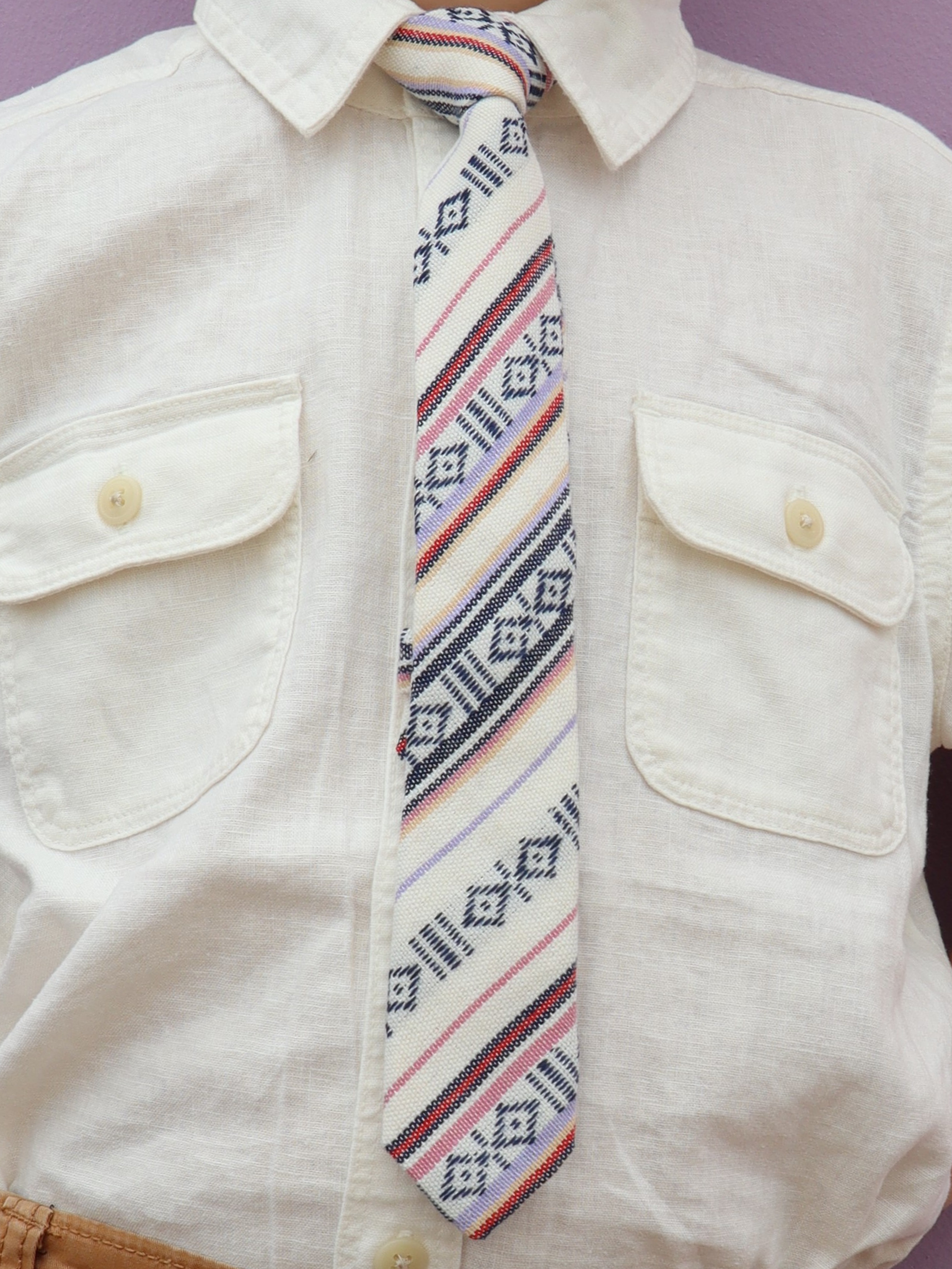 The torso of a boy wearing a striped kids tie with black stripes, pink lines, red bars and Native American inspired designs.