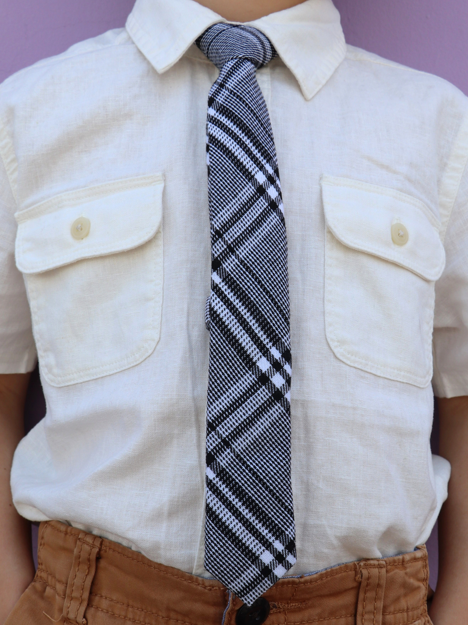 The torso of a boy wearing a plaid kids tie with black plaid pattern with light gray stripes, and diagonal white bars.