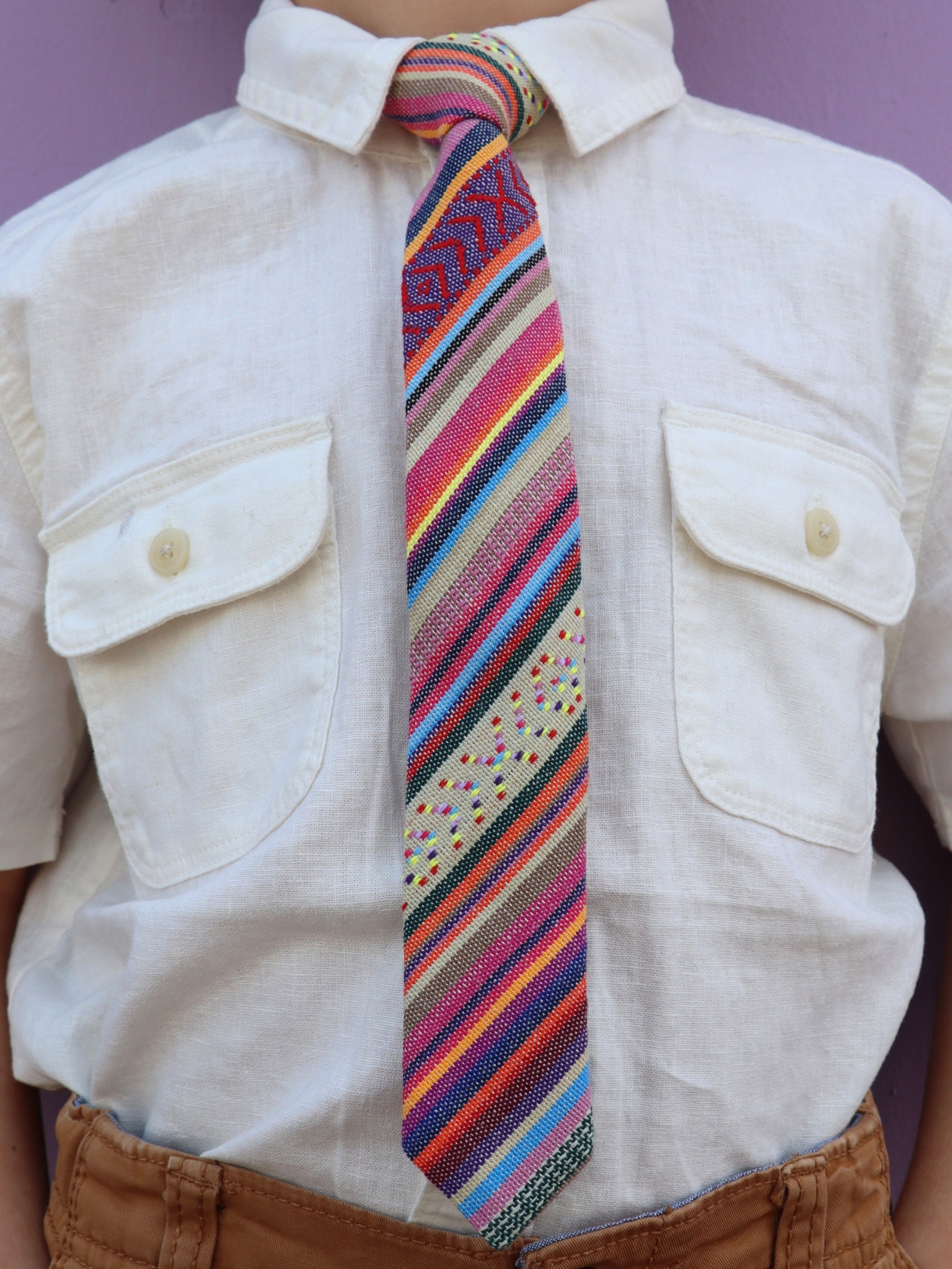 The torso of a boy wearing a striped kids tie with blue stripes, orange lines, red bars and cross designs.