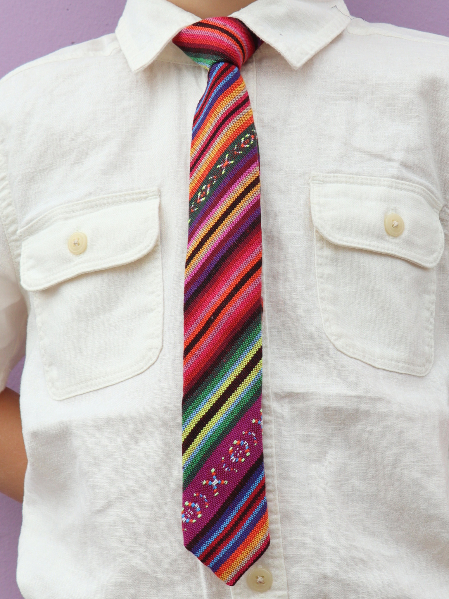 The torso of a boy wearing a striped kids tie with purple stripes, green and yellow lines, orange and red bars.